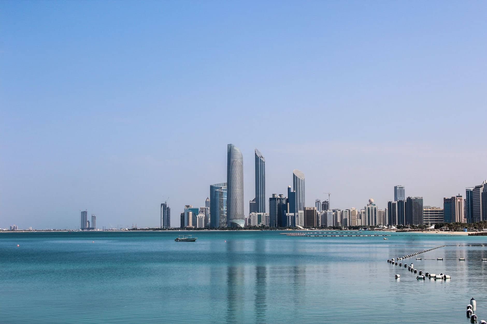 Stunning view of the Abu Dhabi skyline reflecting in the calm Gulf waters on a sunny day.