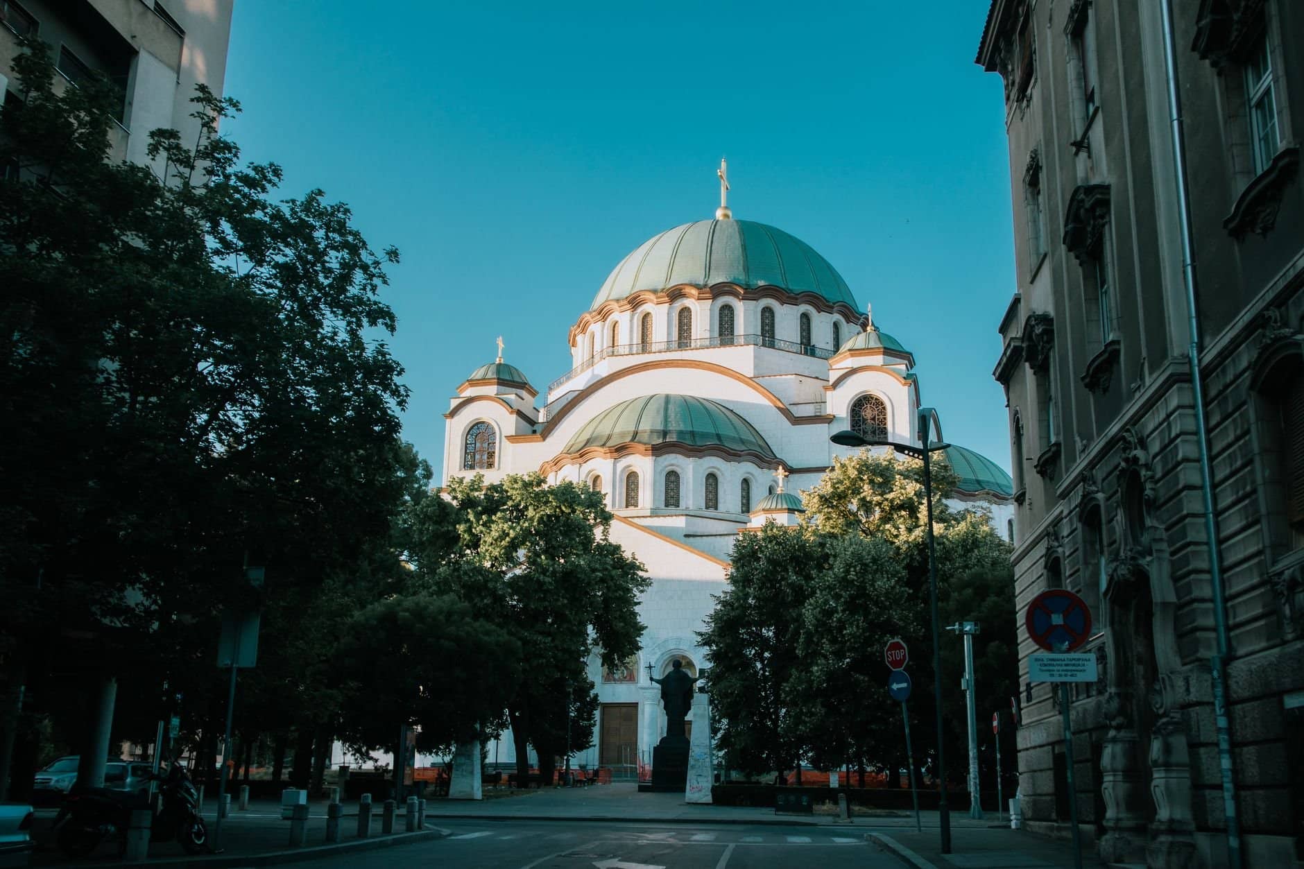 View of the iconic Saint Sava Temple in Belgrade on a sunny day, framed by trees and buildings.