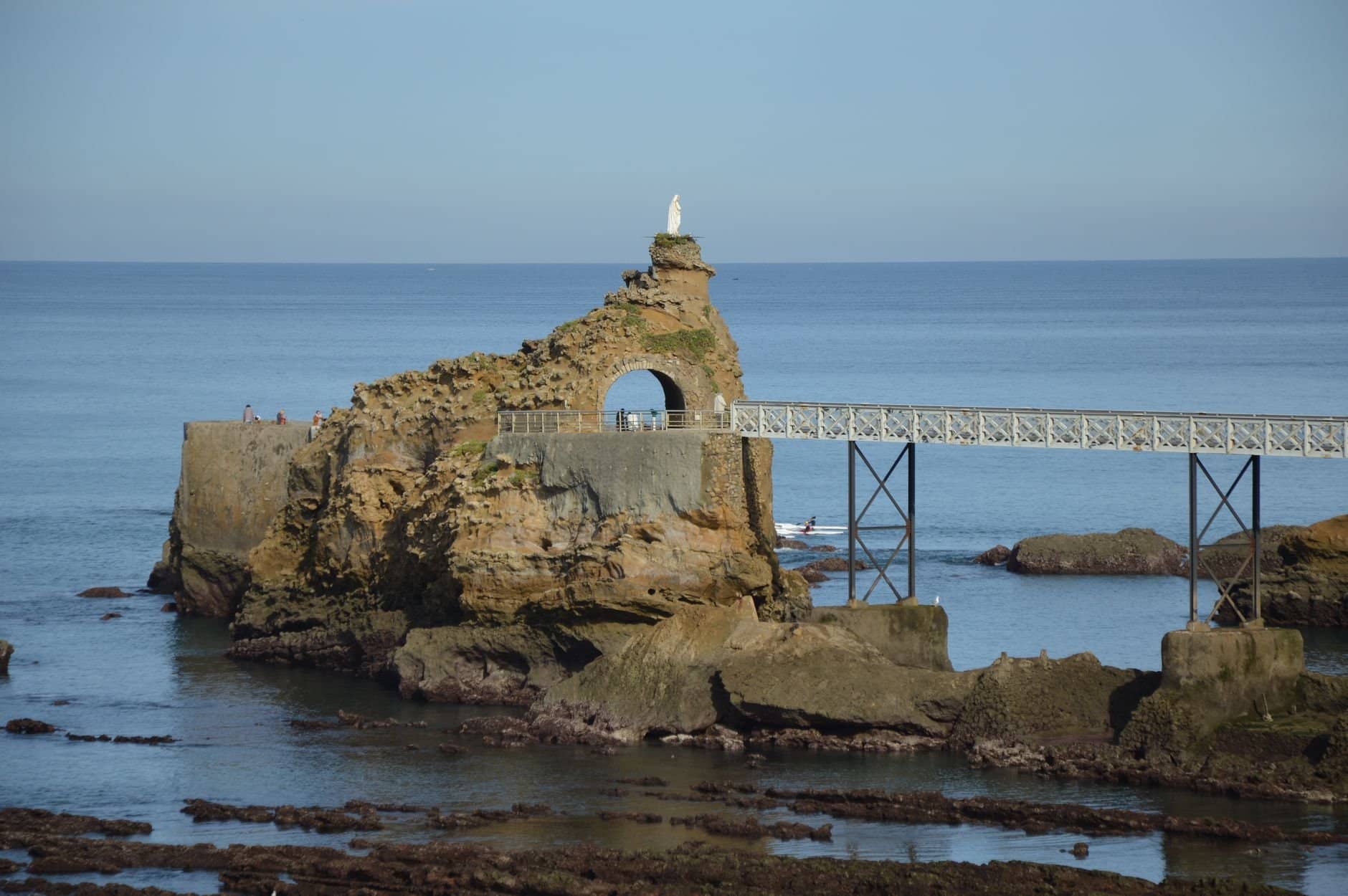 Rock formation with arch bridge and statue in Biarritz, overlooking the sea.