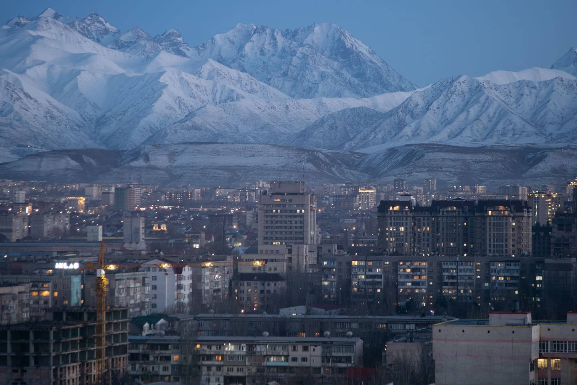 Stunning aerial view of Bishkek city against a backdrop of snow-covered mountains during twilight.