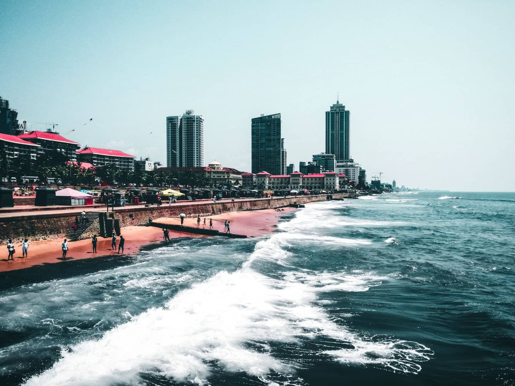 Scenic view of a coastal city with tall buildings and waves crashing against the shore.