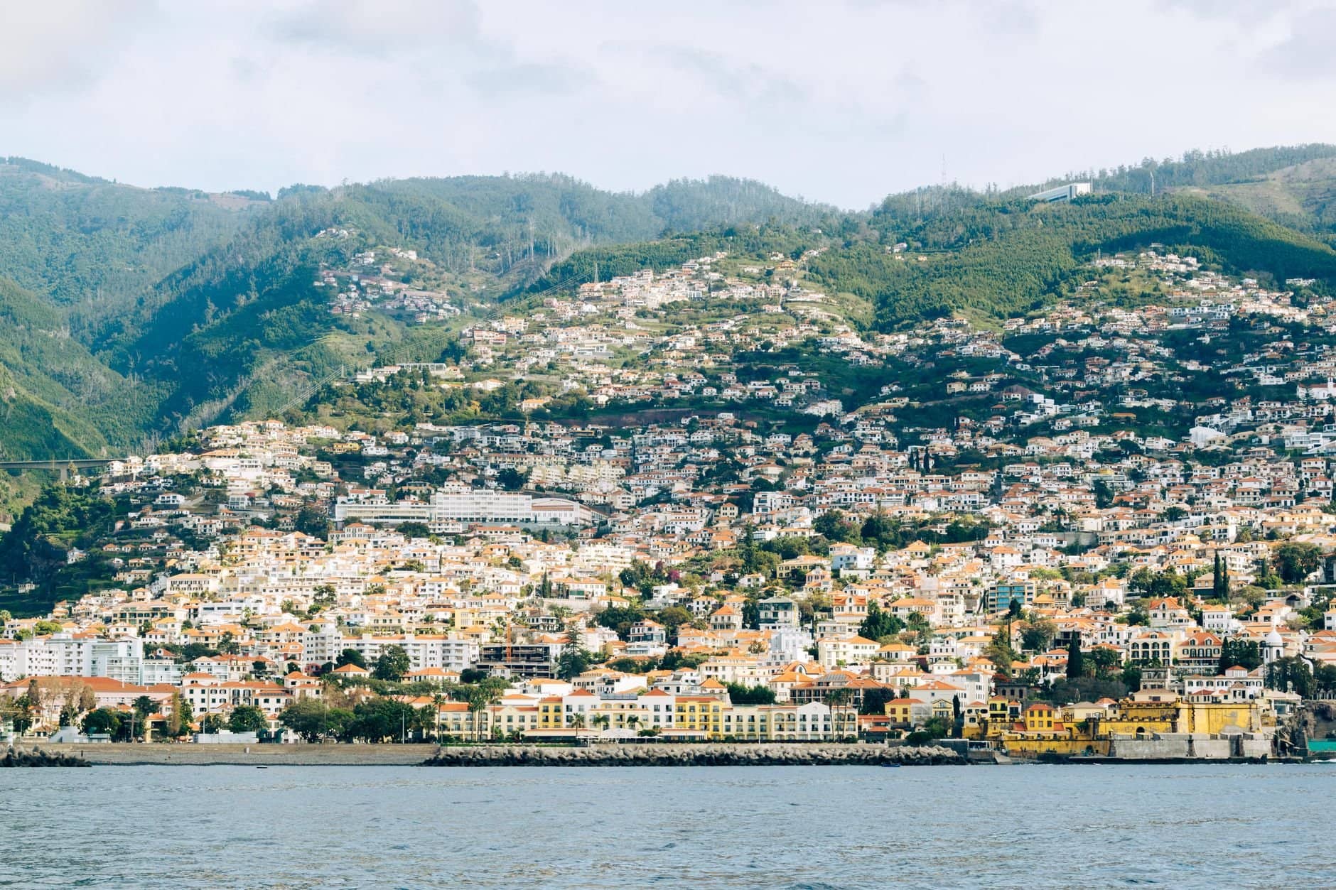 Scenic view of Madeira's hillside urban landscape with vibrant architecture and lush green hills.