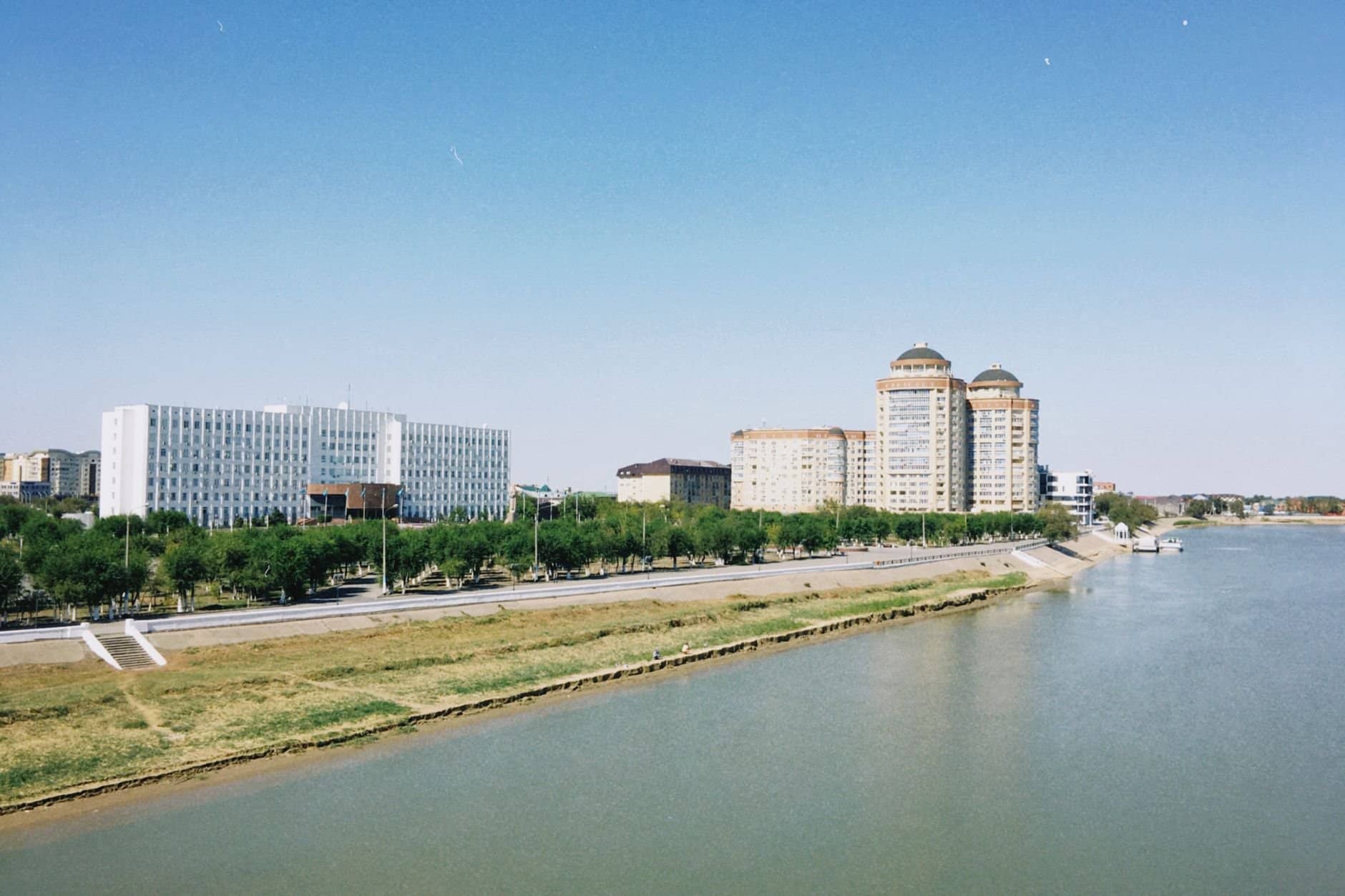 A scenic daytime view of Atyrau city skyline with modern buildings along the Ural River in Kazakhstan.