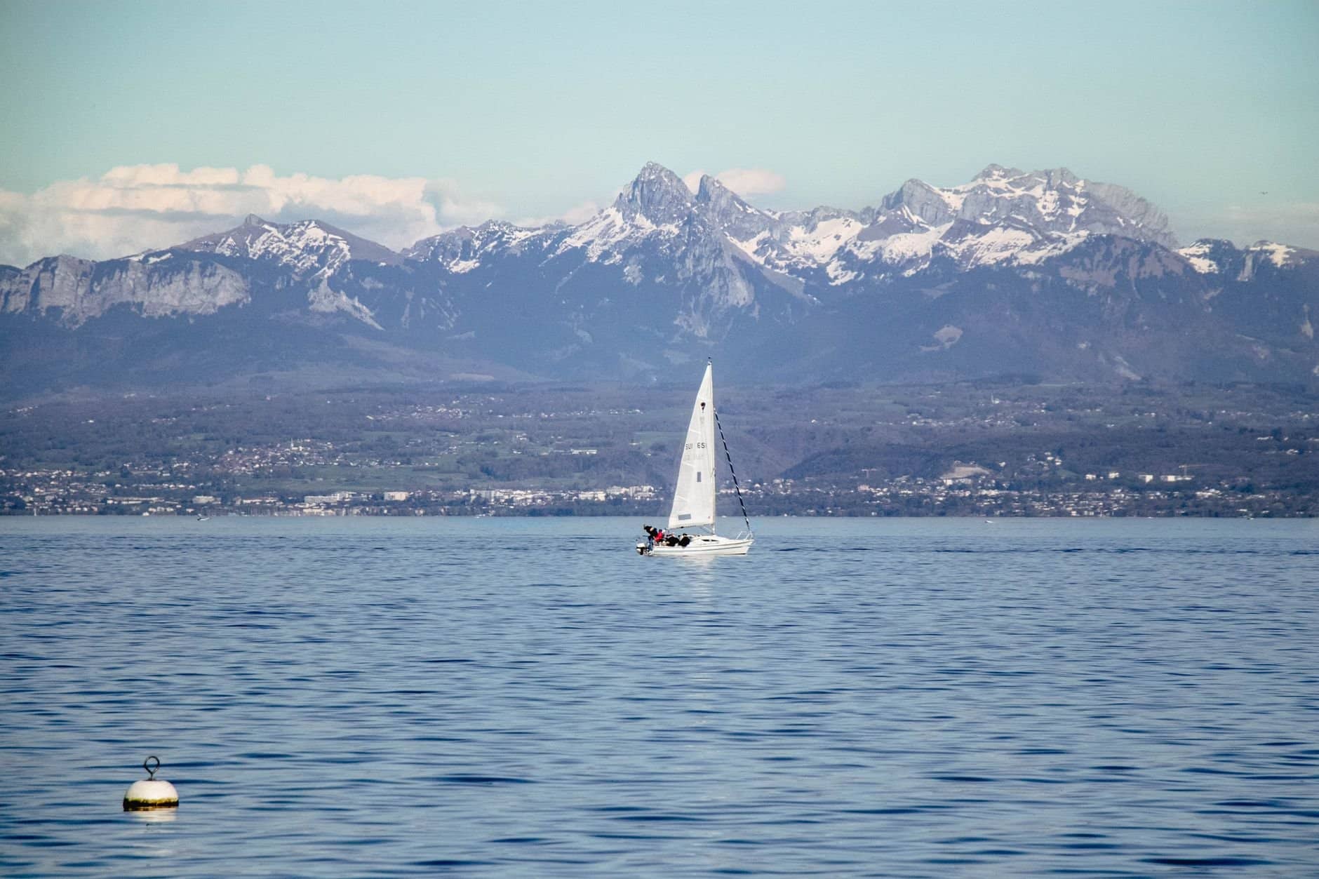 A sailboat glides on Lake Geneva with the majestic Alps in the background, capturing serene nature.
