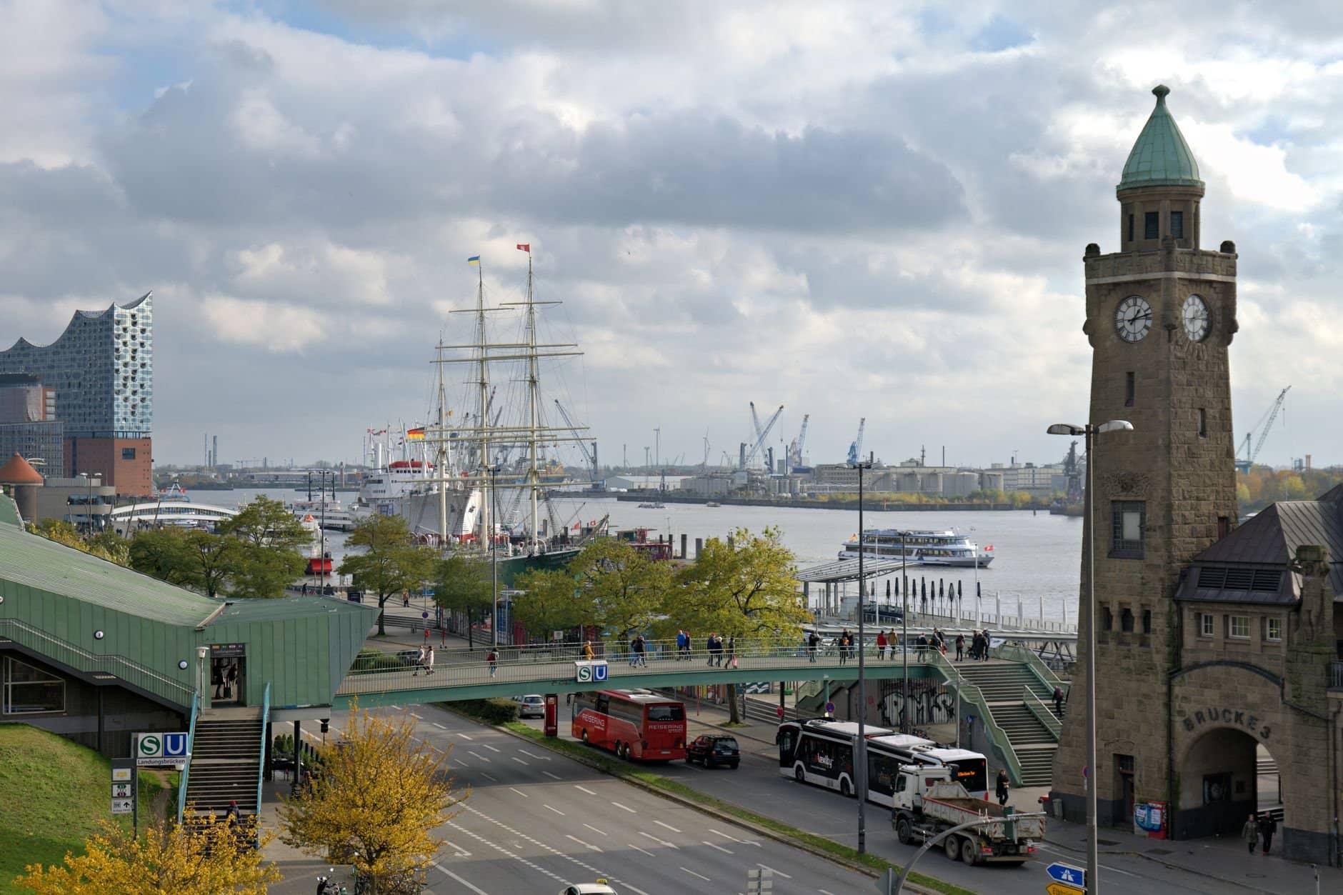 A busy day at Hamburg's harbor featuring the Elbphilharmonie, historic ships, and clock tower.