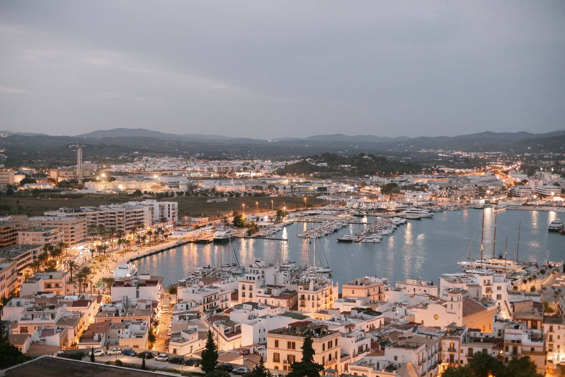 A scenic aerial view of Ibiza's marina at dusk, showcasing vibrant city lights and bustling harbor in Spain.