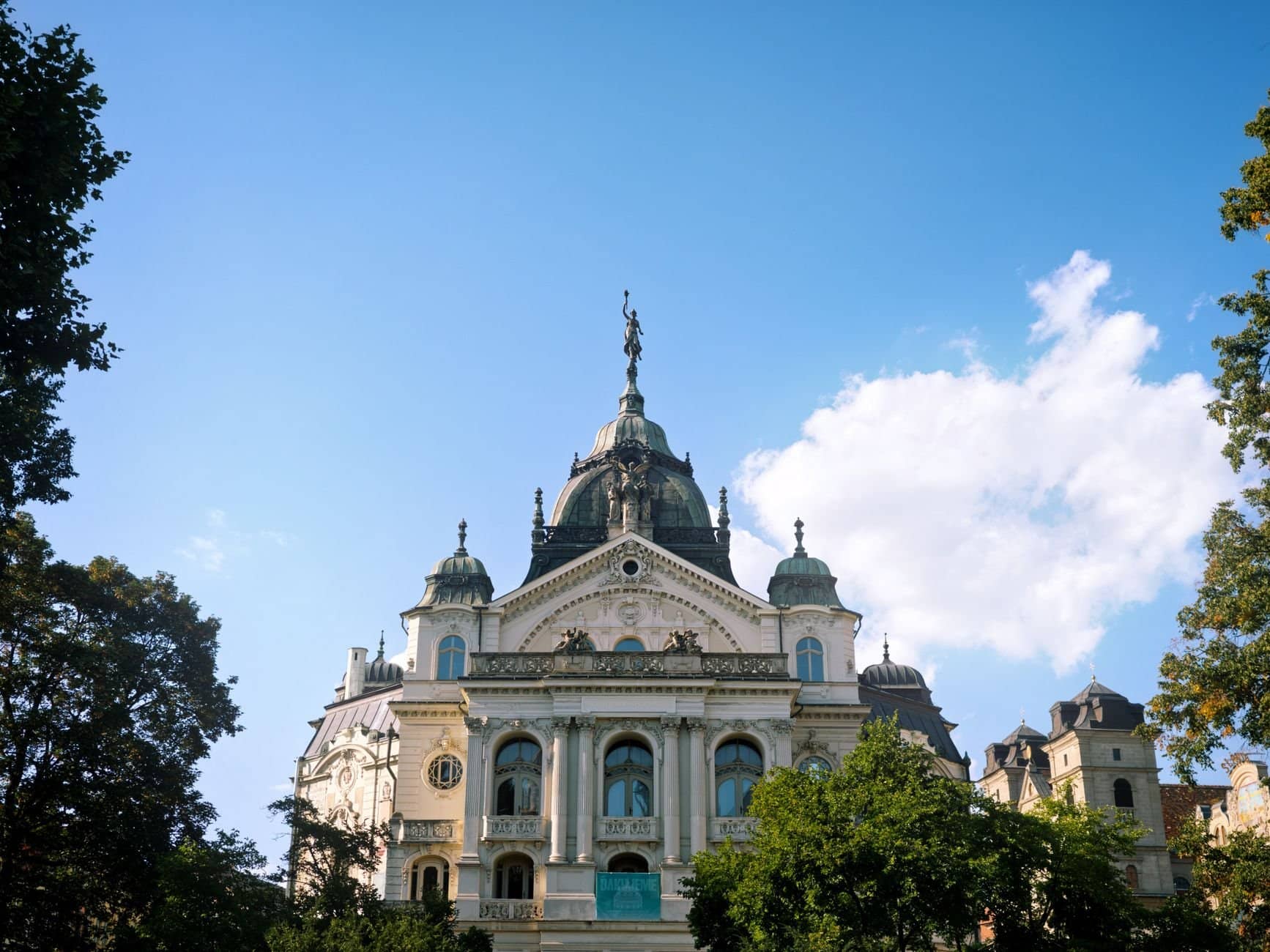 A grand historical building with domes and statues against a clear blue sky, surrounded by trees.