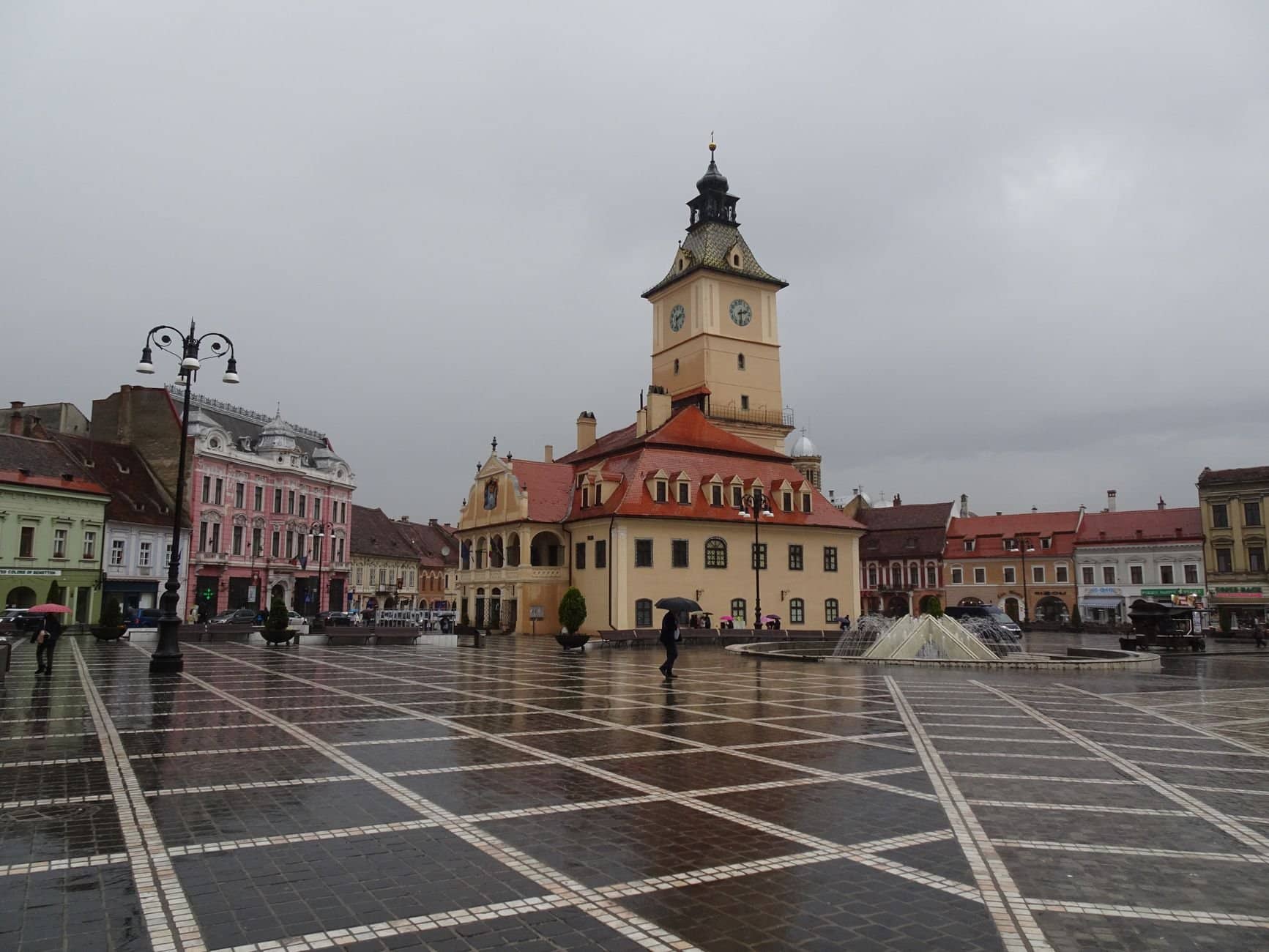 Explore the charm of Brașov's medieval town square under a cloudy sky with historic architecture.