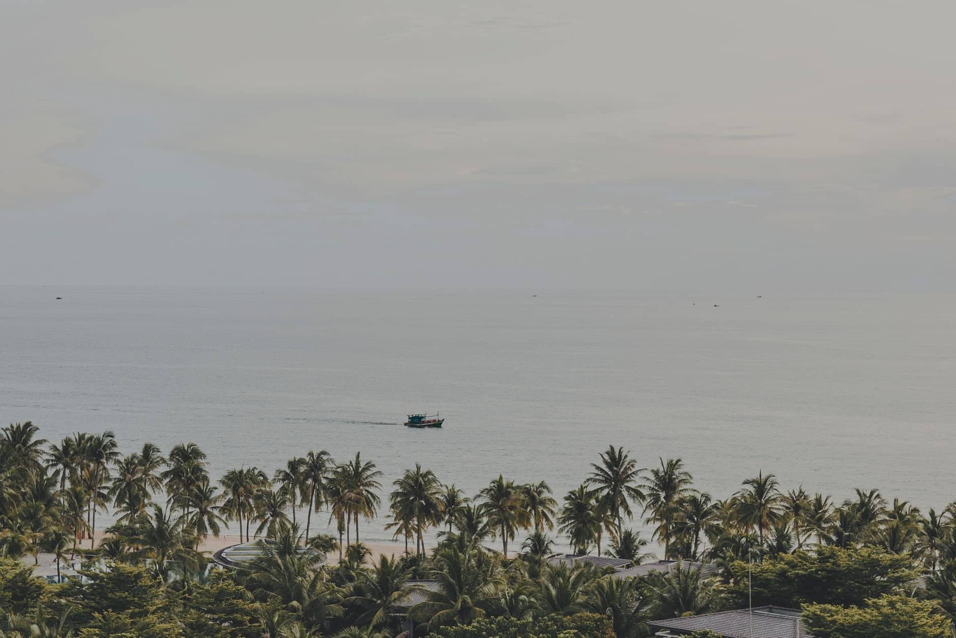 Serene panorama of palm-lined Phu Quoc beach with a distant boat on the calm sea.