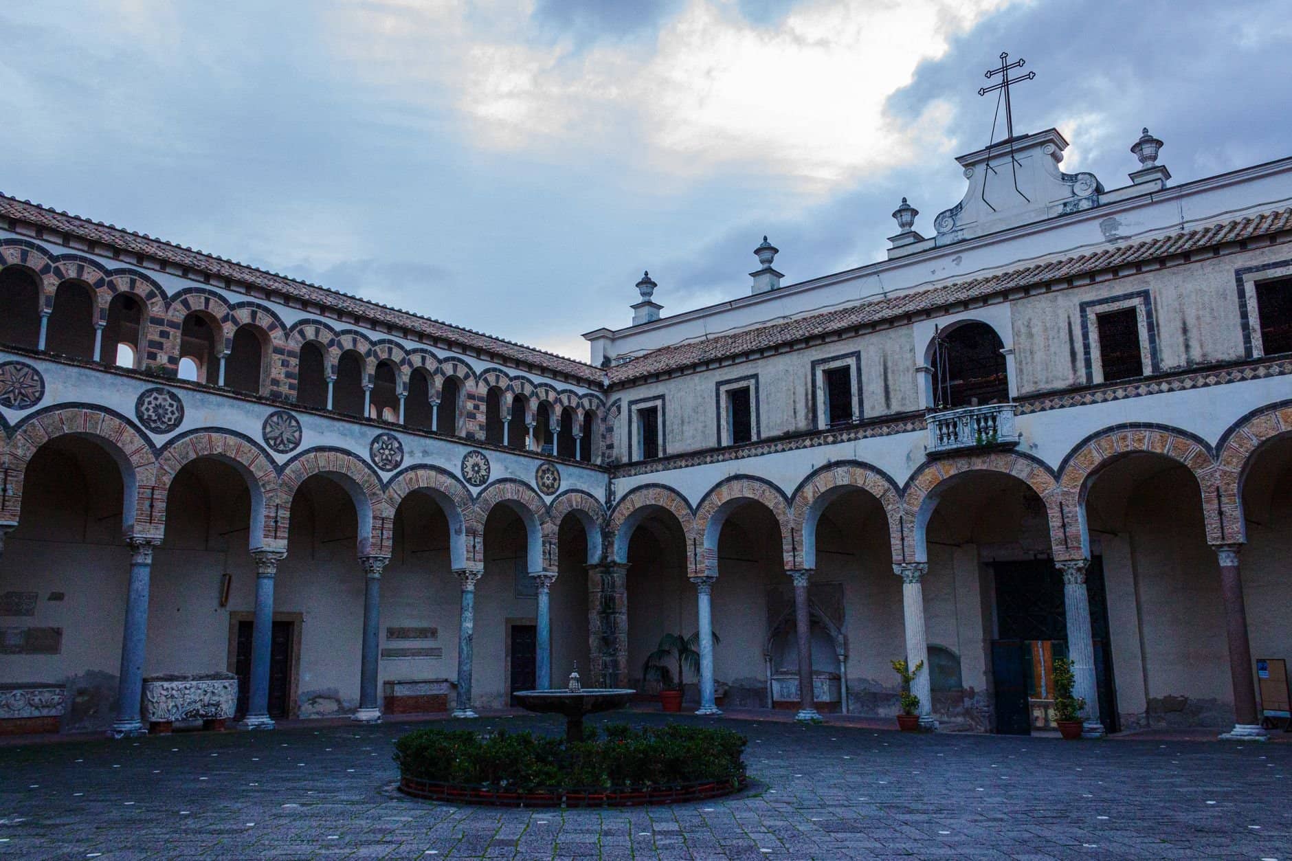 Scenic view of a historical cloister in Salerno with arches and religious symbols.