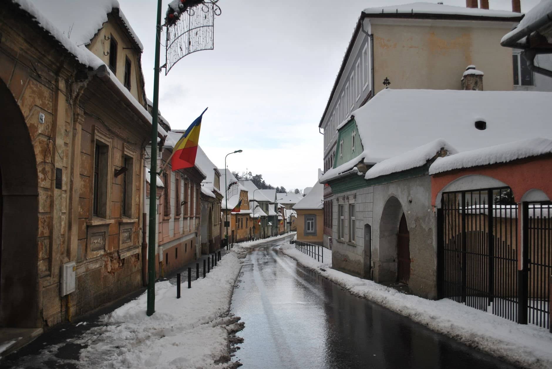 A picturesque snowy street in a historic town with Romanian architectural charm and a Romanian flag.
