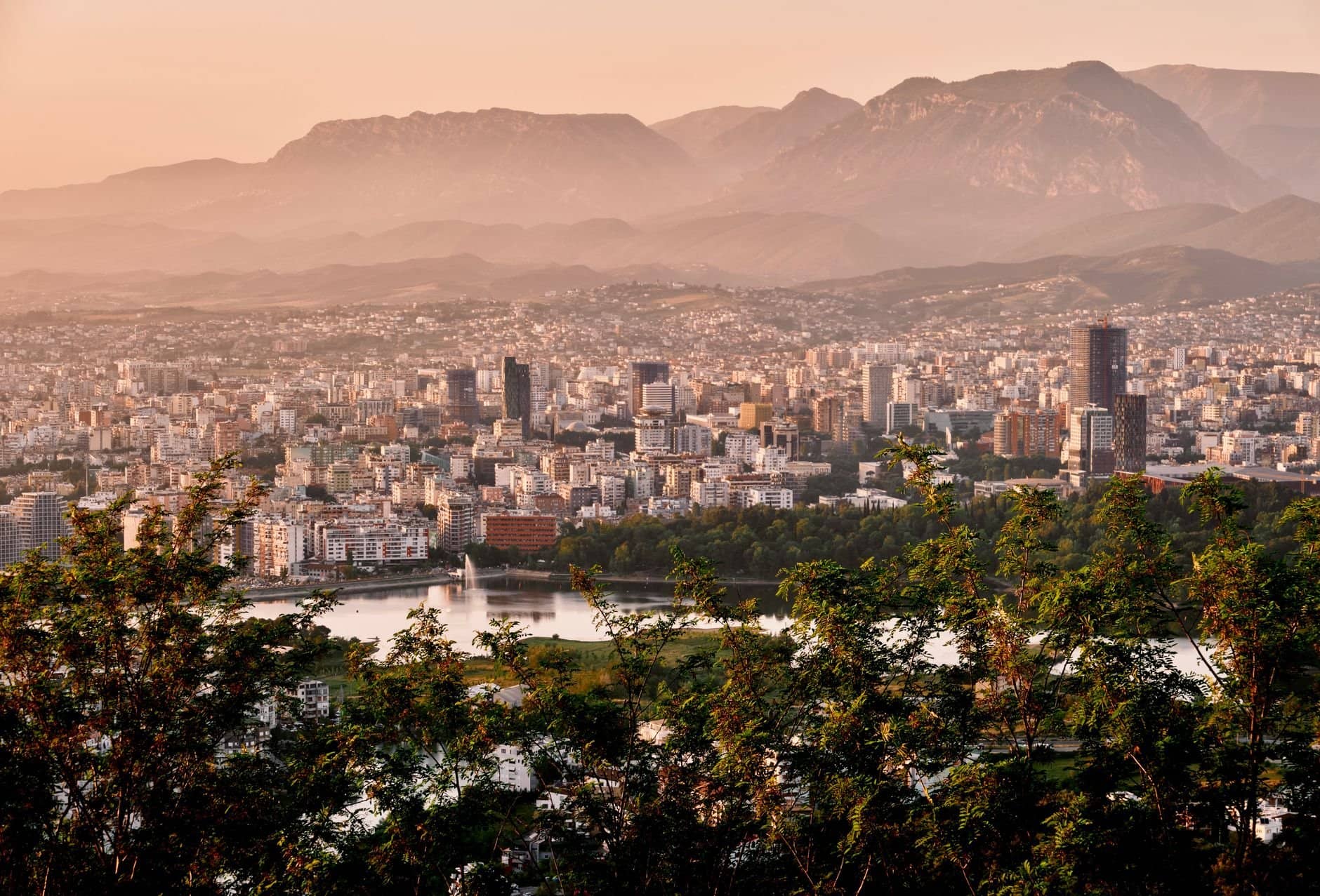 A stunning aerial view of Tirana's skyline framed by mountains and lush greenery during sunset.