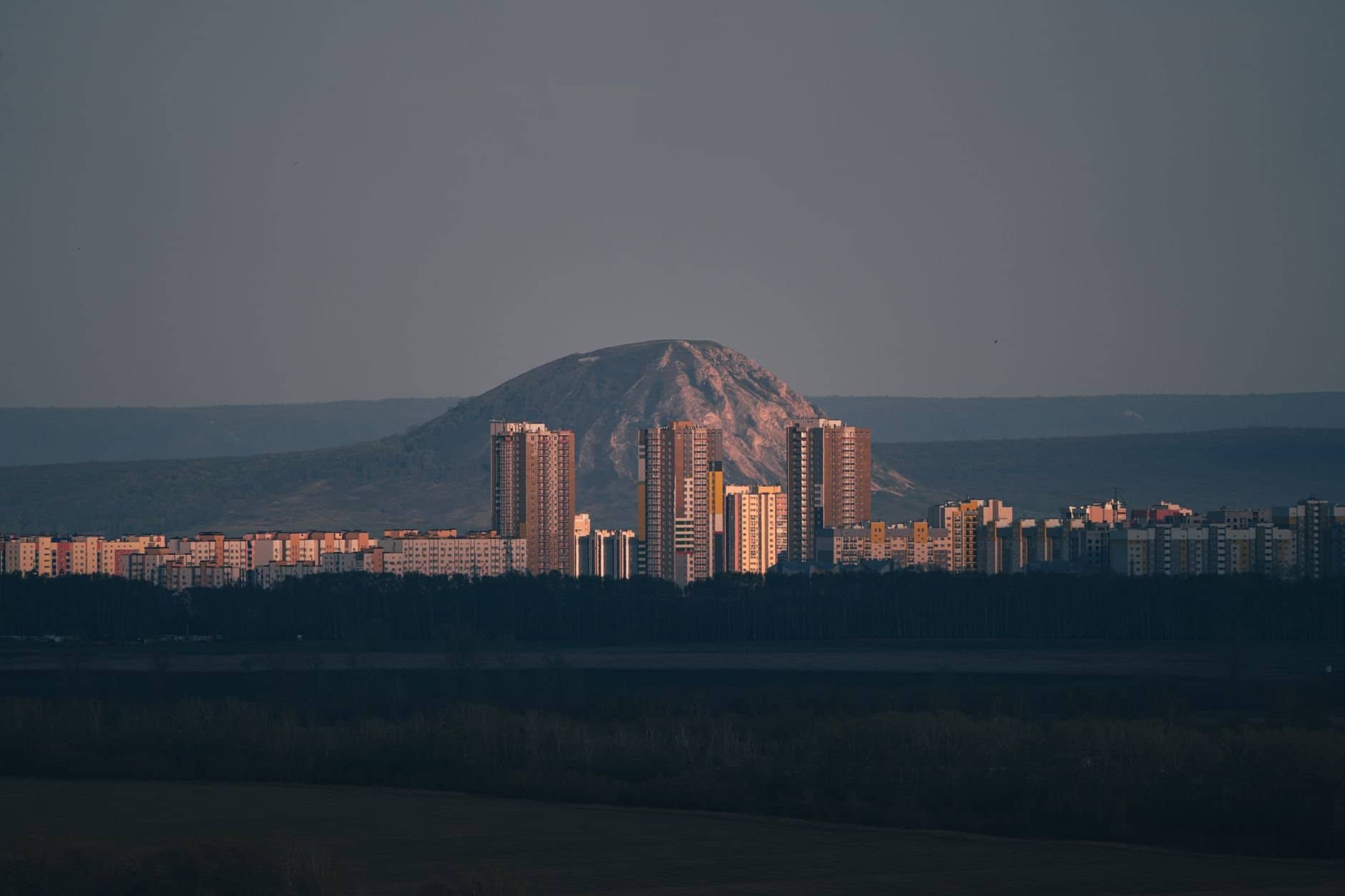 A stunning cityscape of Ufa at dusk showcasing high-rise buildings and a mountain backdrop.