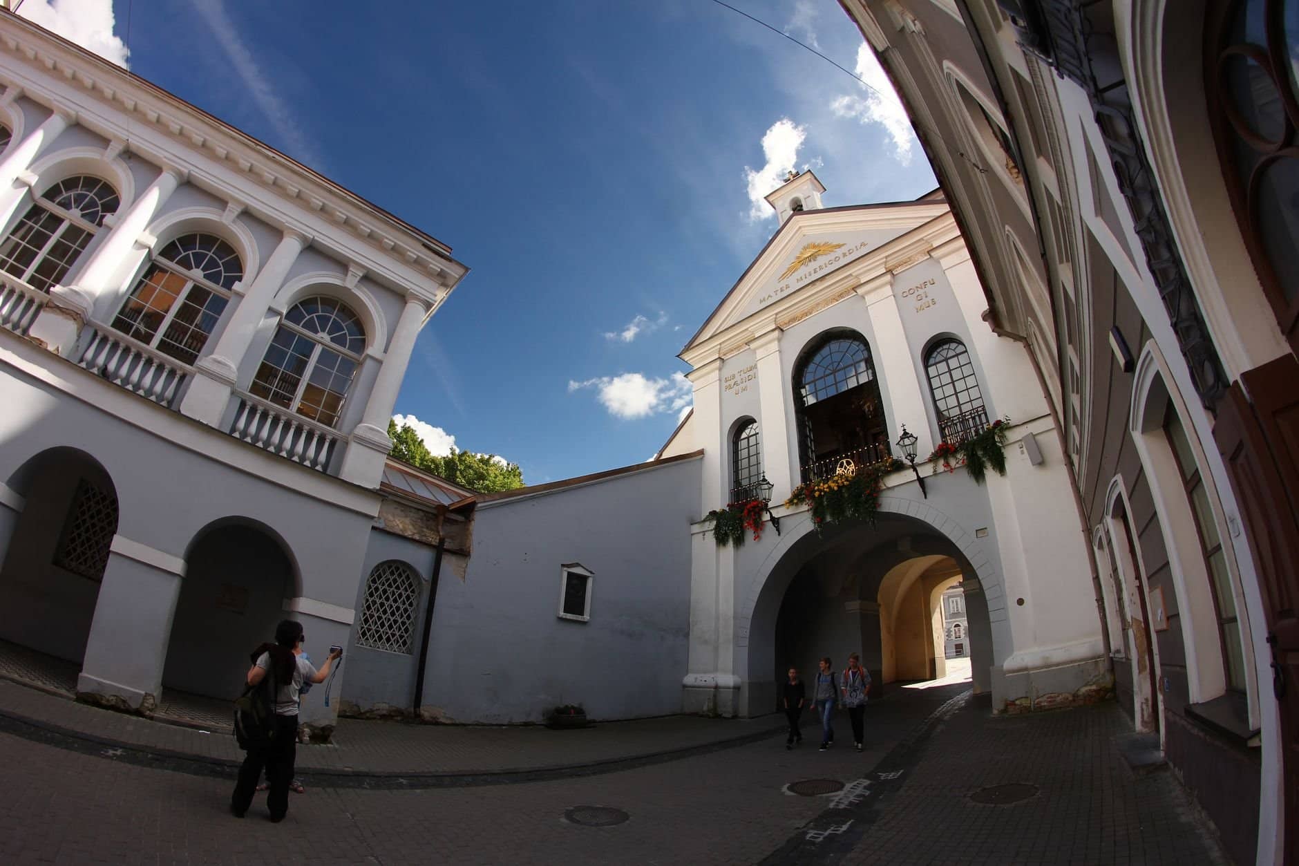Tourists exploring the historic Gates of Dawn in Vilnius, Lithuania on a sunny day.