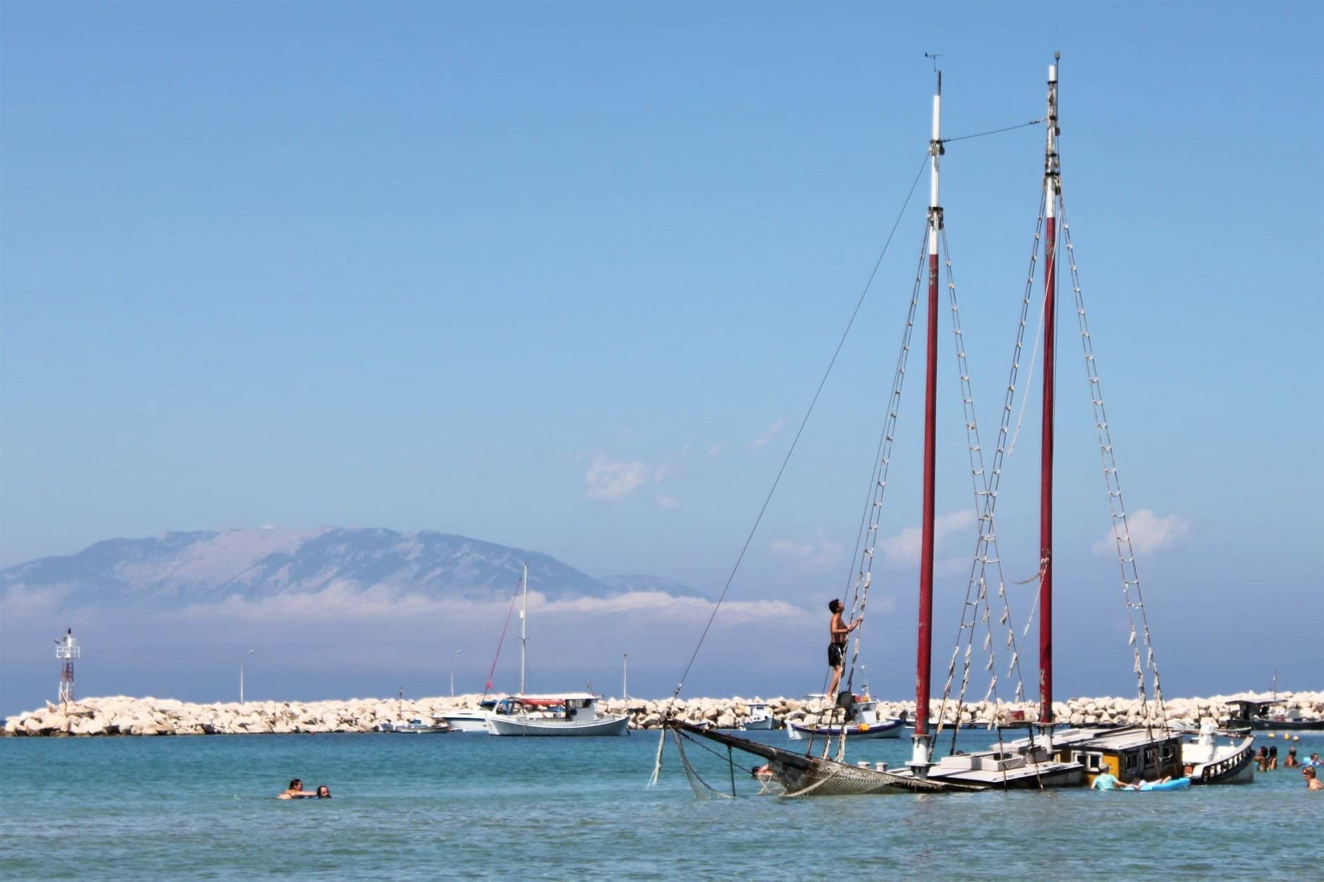 Enjoy a sunny day at Zakinthos harbor with sailboats and swimmers.