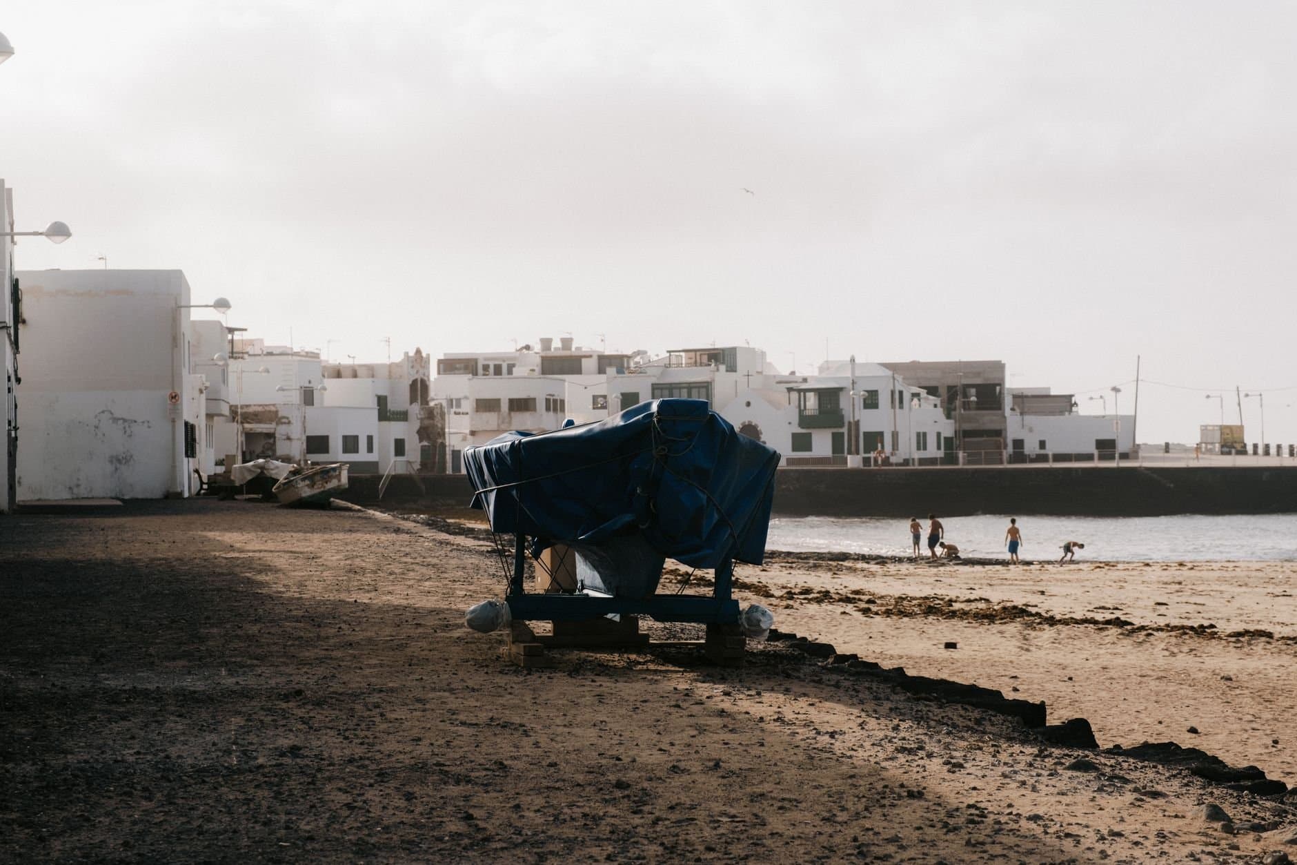 A serene beach scene in Arrecife, Lanzarote with weathered buildings and covered cart.