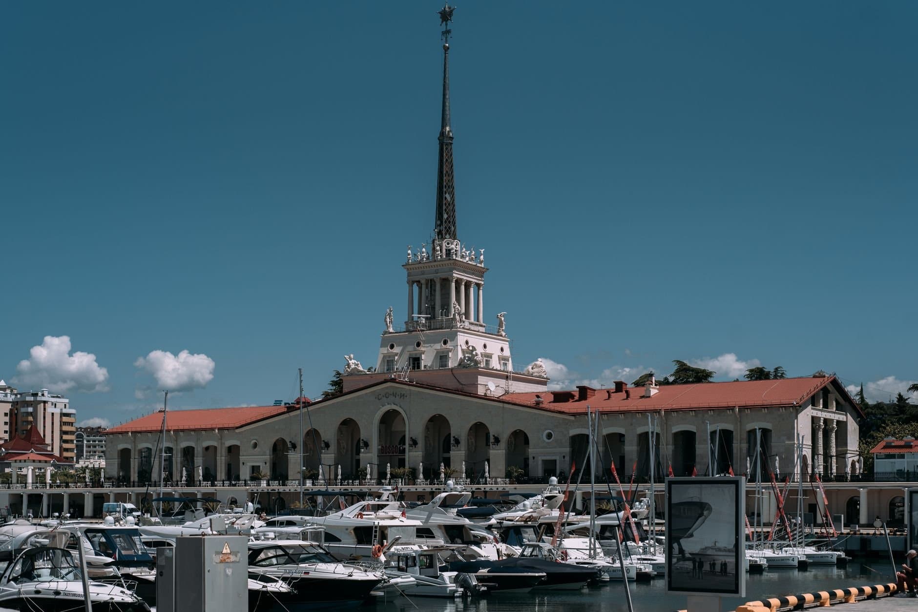 Charming view of the Sochi Marina with yachts and iconic tower on a sunny day.