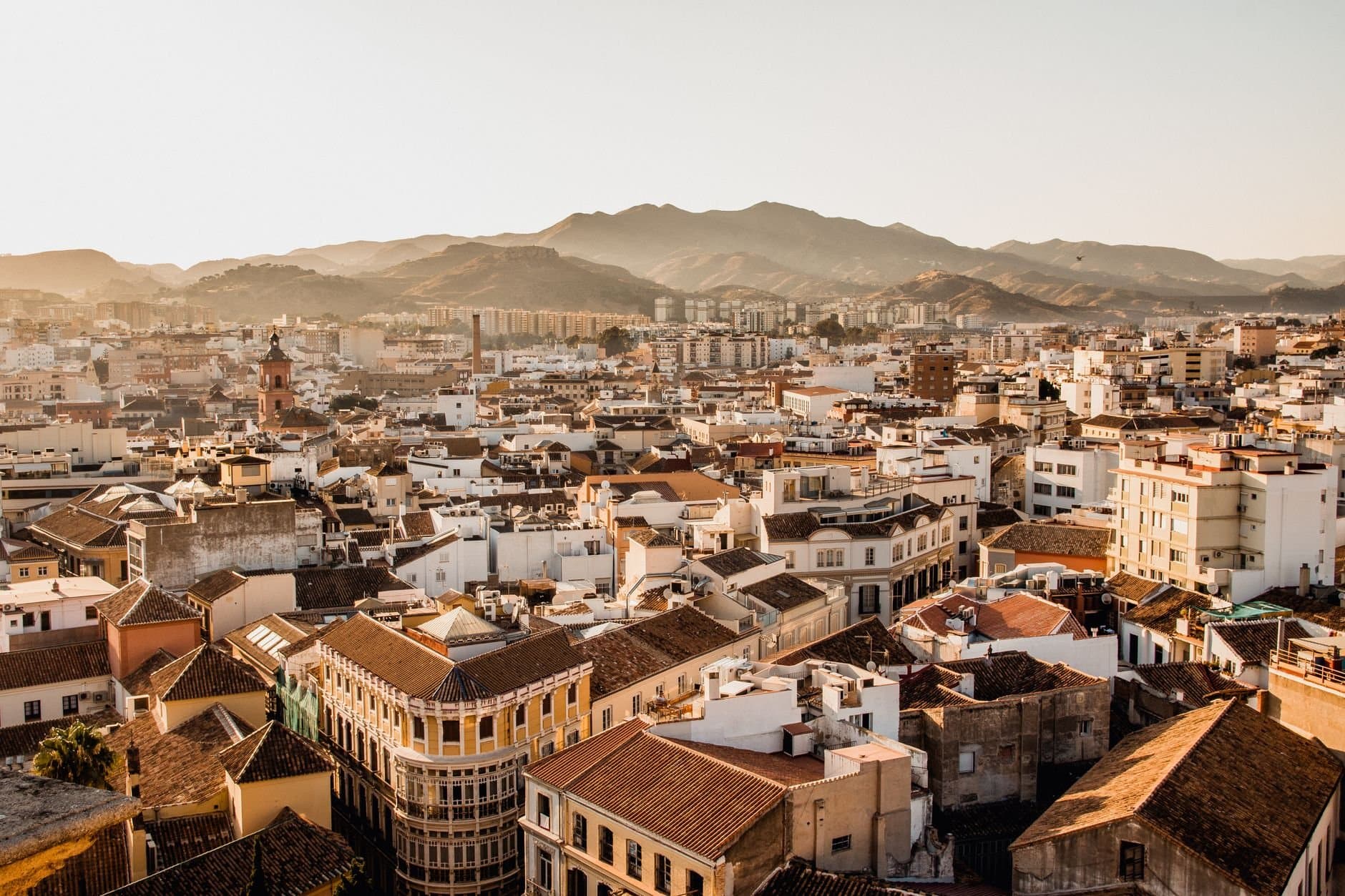 Aerial view of Málaga's cityscape with mountains in the background during sunset.