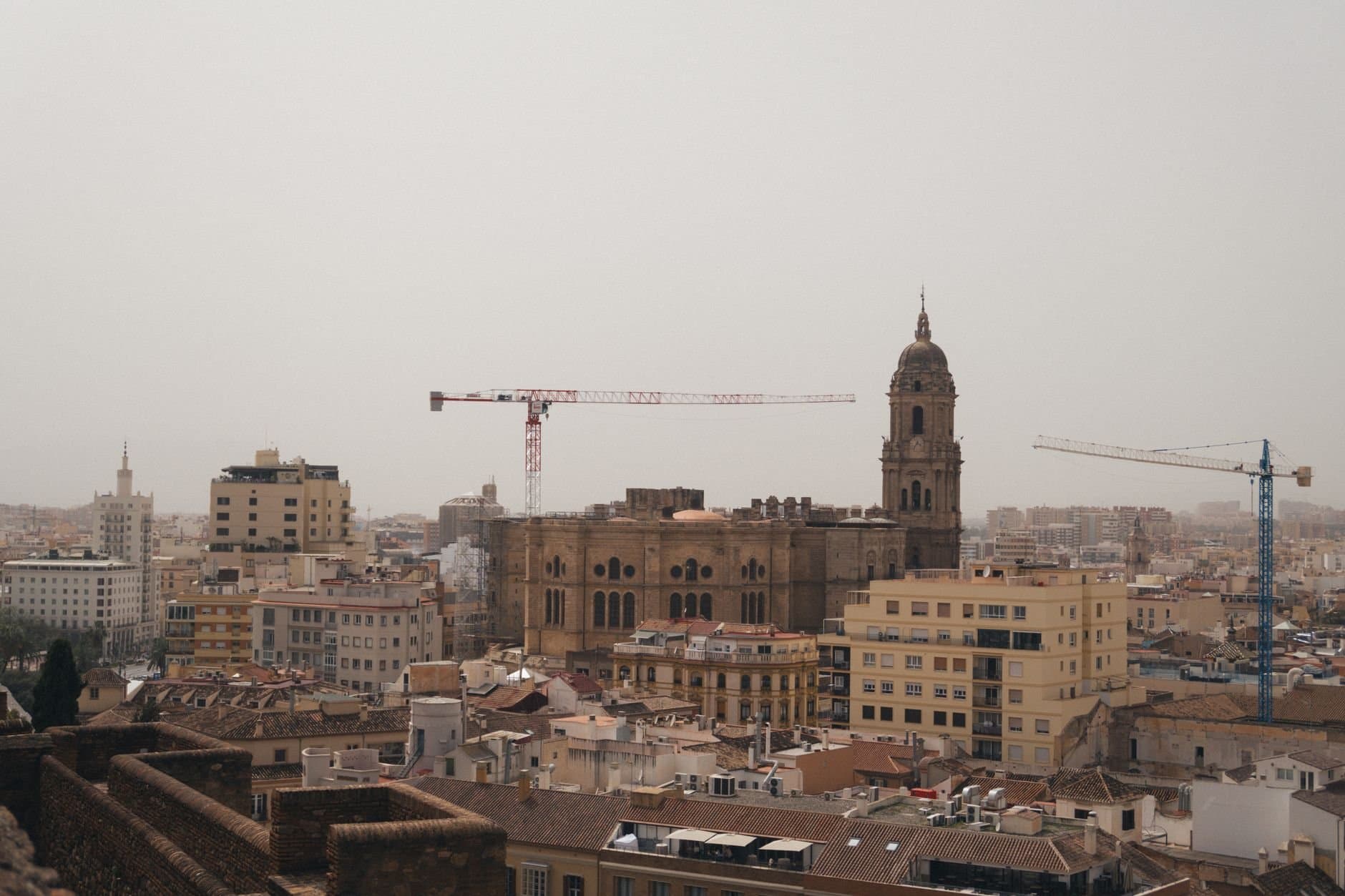 A stunning urban landscape featuring Malaga Cathedral amidst cranes and city buildings.