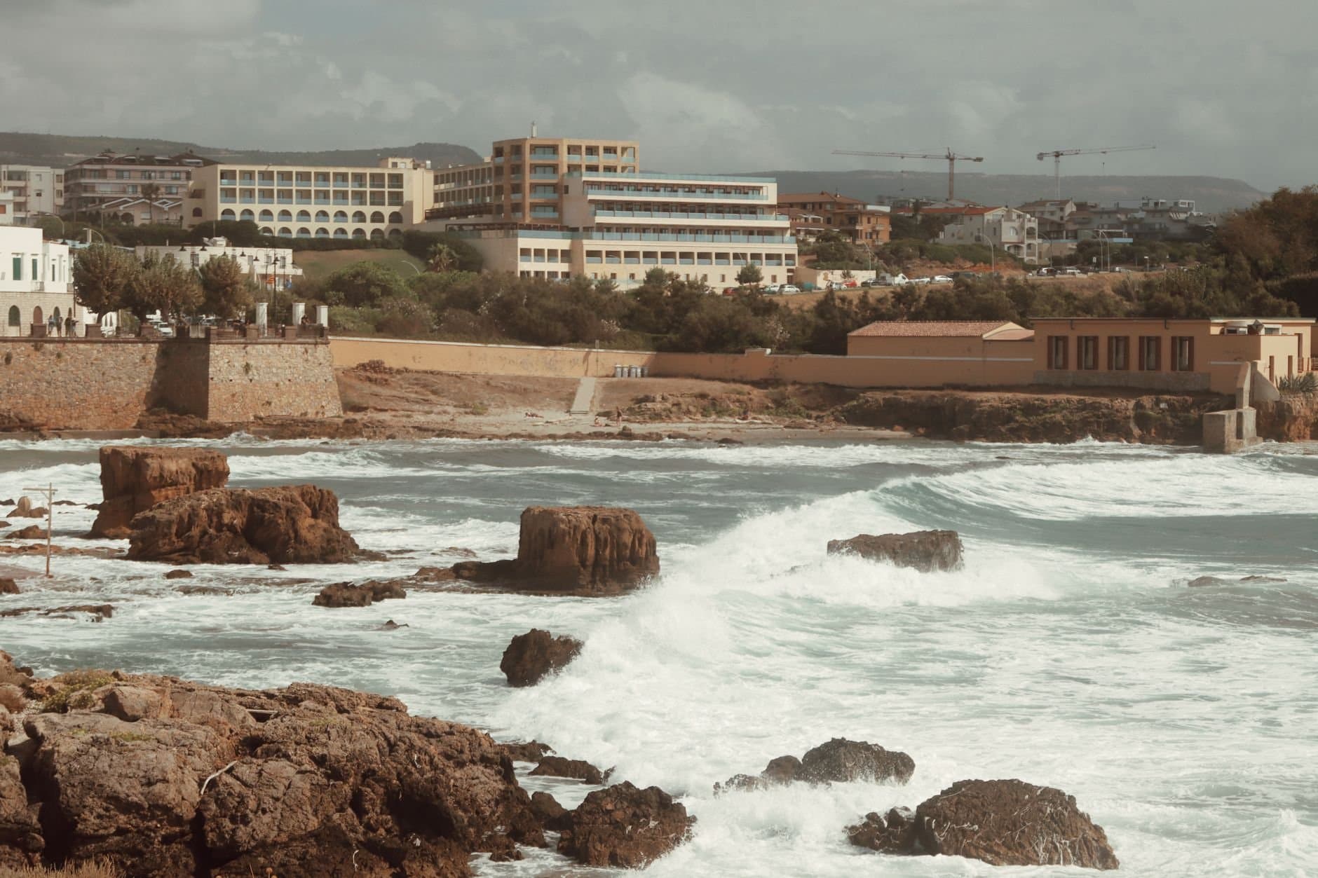 Explore the rugged coastline of Alghero, Sardinia with its historic architecture and waves crashing on rocky shores.