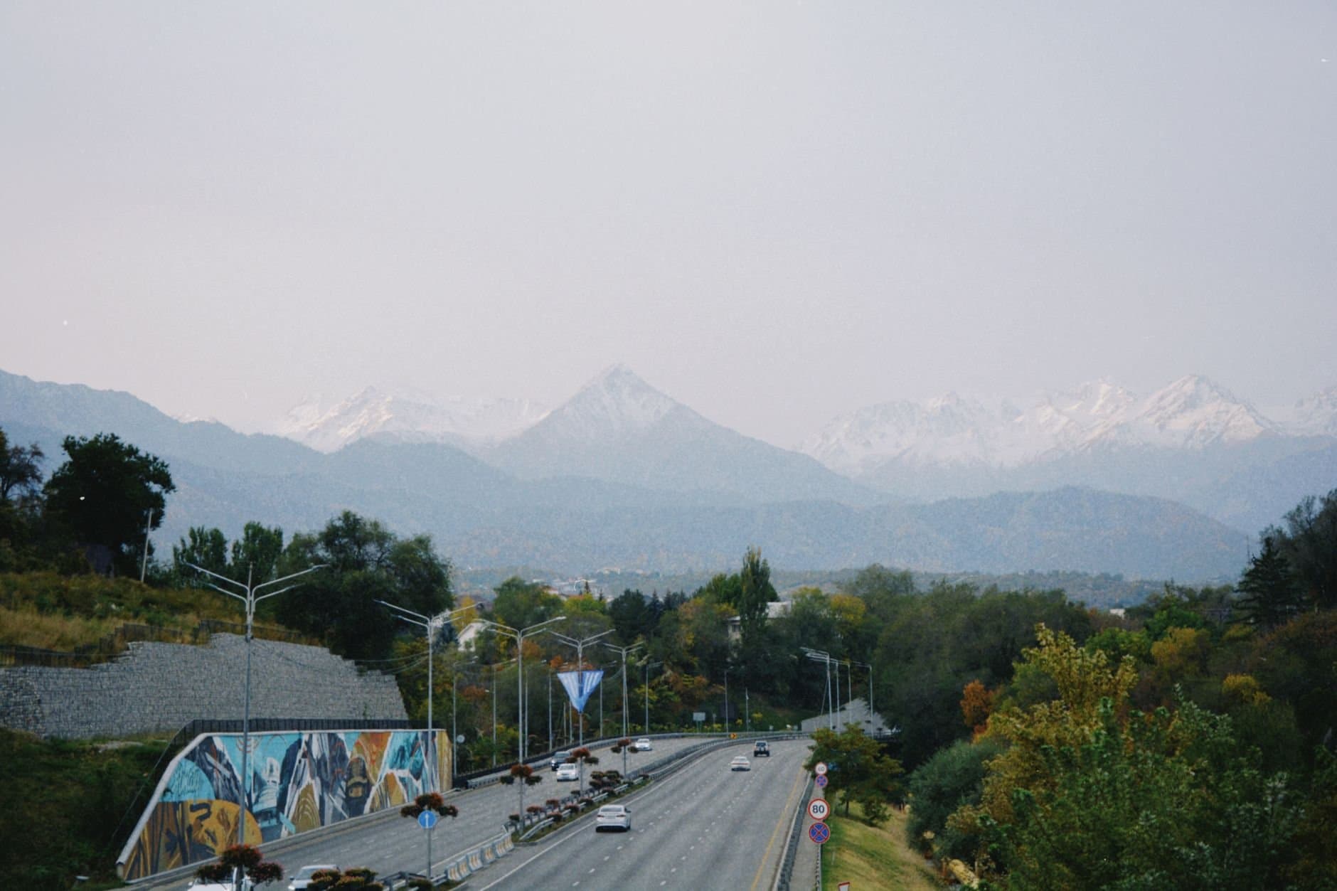 A picturesque road in Almaty, Kazakhstan, with stunning mountain backdrop and vibrant autumn foliage.