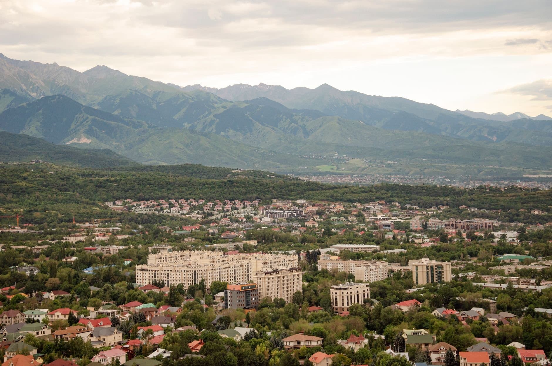 A panoramic view of Almaty city with lush greenery and mountains in the background.