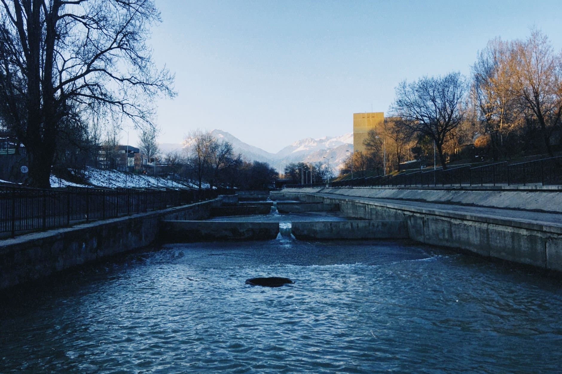 Serene river scene in Almaty, Kazakhstan, framed by snowy mountains and winter trees.