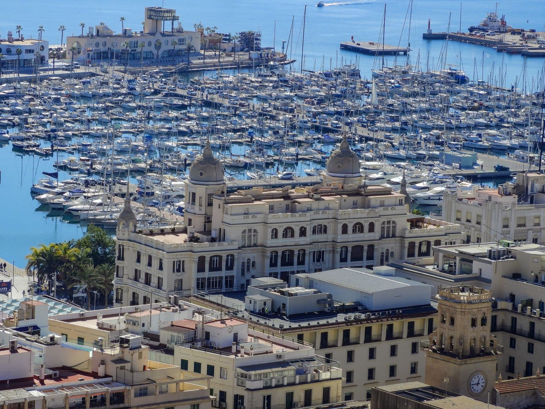 Aerial view of Alicante marina with boats and historic architecture under a clear blue sky.