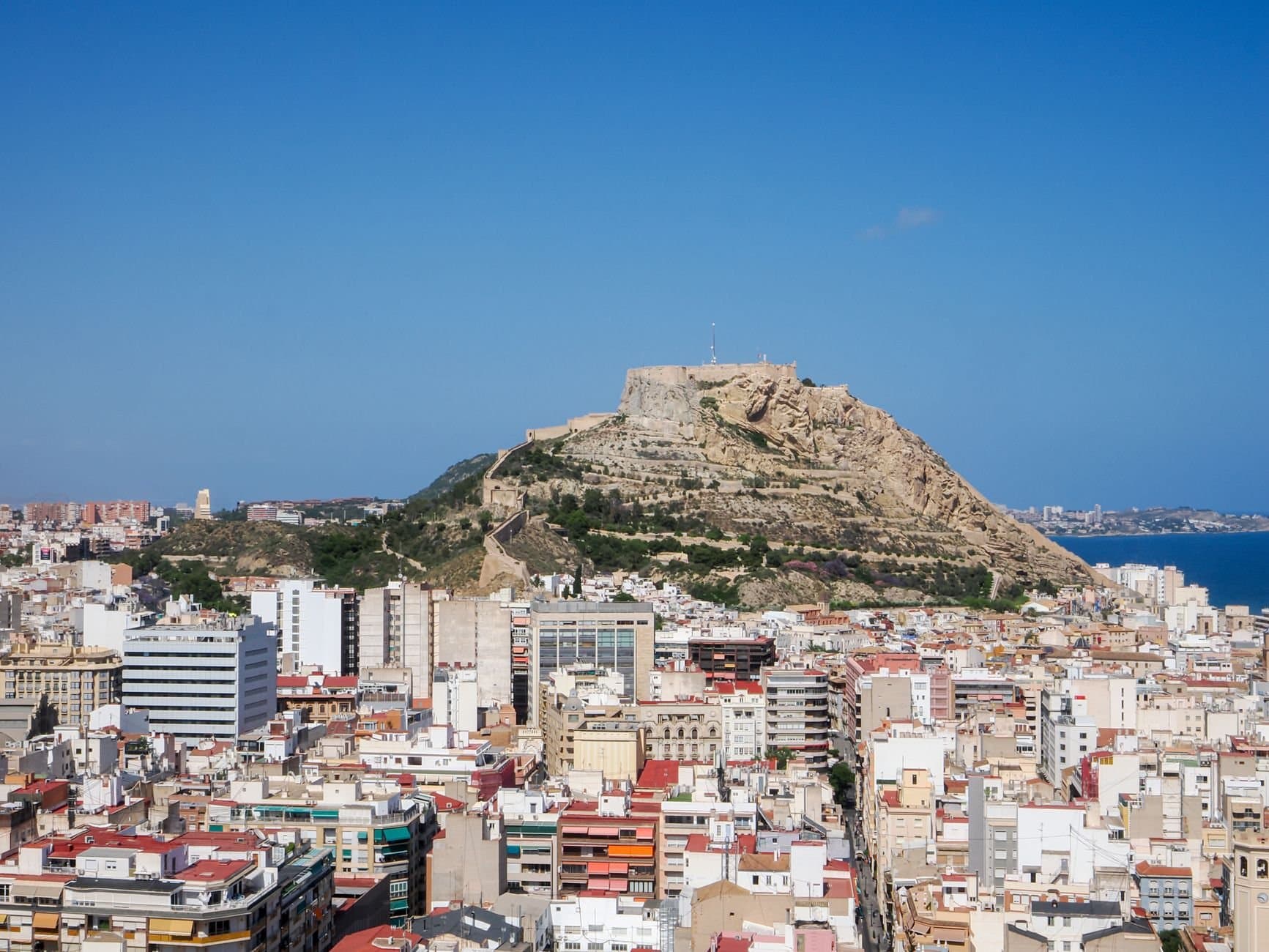 A panoramic view of Alicante showcasing the Santa Bárbara Castle on the hilltop under a clear blue sky.