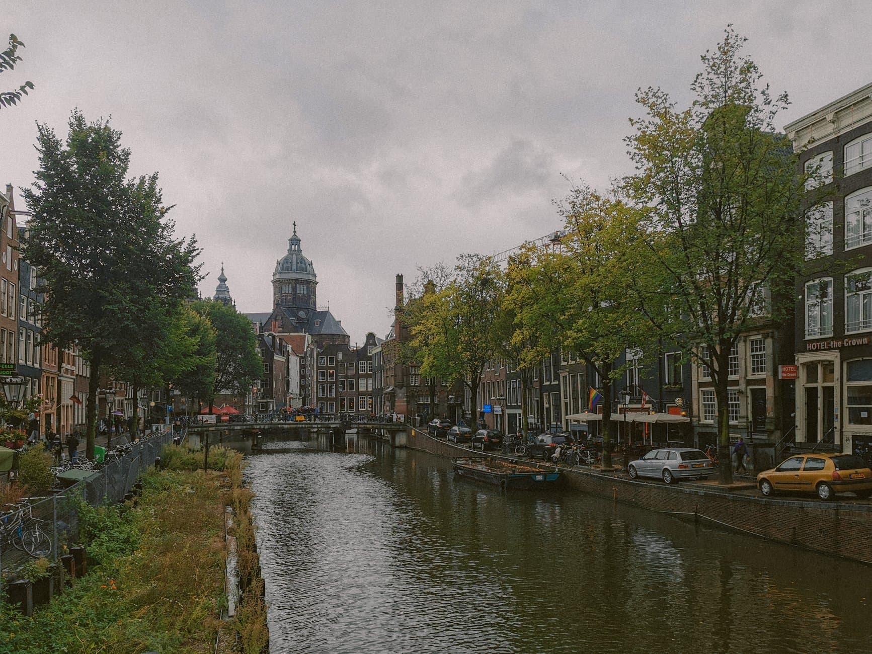 Scenic view of Amsterdam's canal with historic buildings and cathedral on a cloudy day.