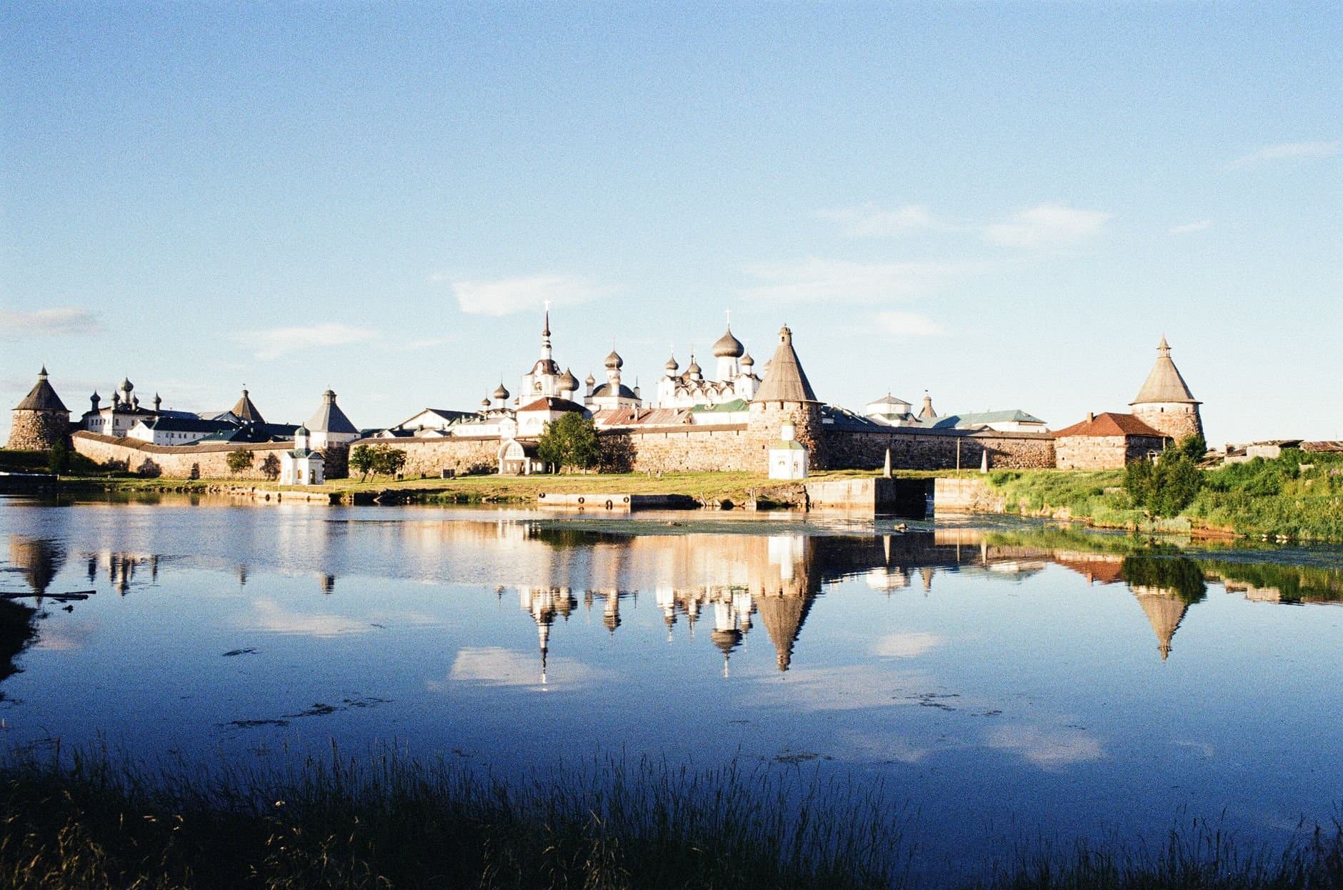 Scenic view of the Solovetsky Monastery reflected in a serene lake under a clear sky.