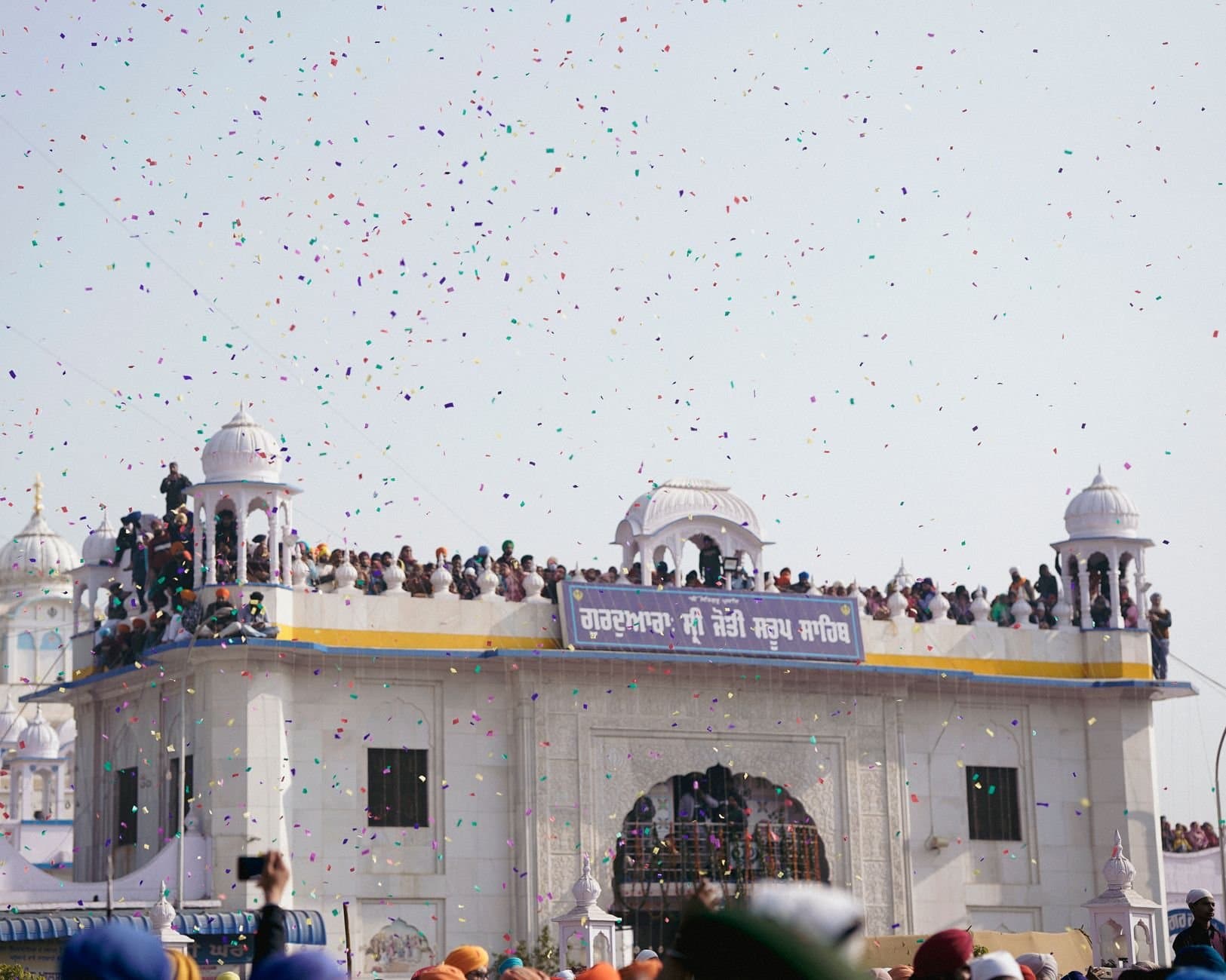 Crowds gather at a classic dome for a traditional festival with colorful confetti in the air.