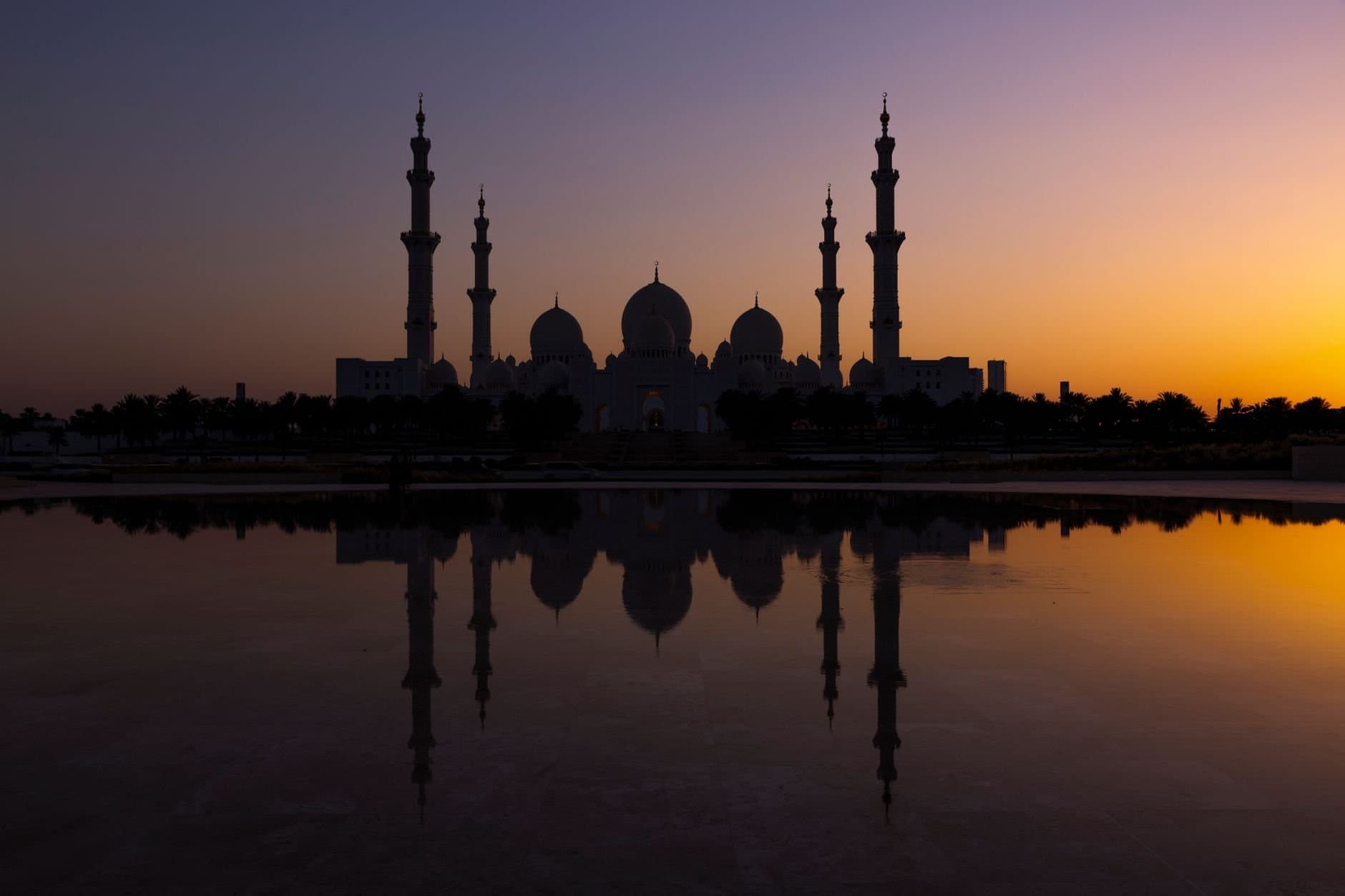 Silhouette of Sheikh Zayed Grand Mosque reflecting in water during a vibrant sunset in Abu Dhabi.