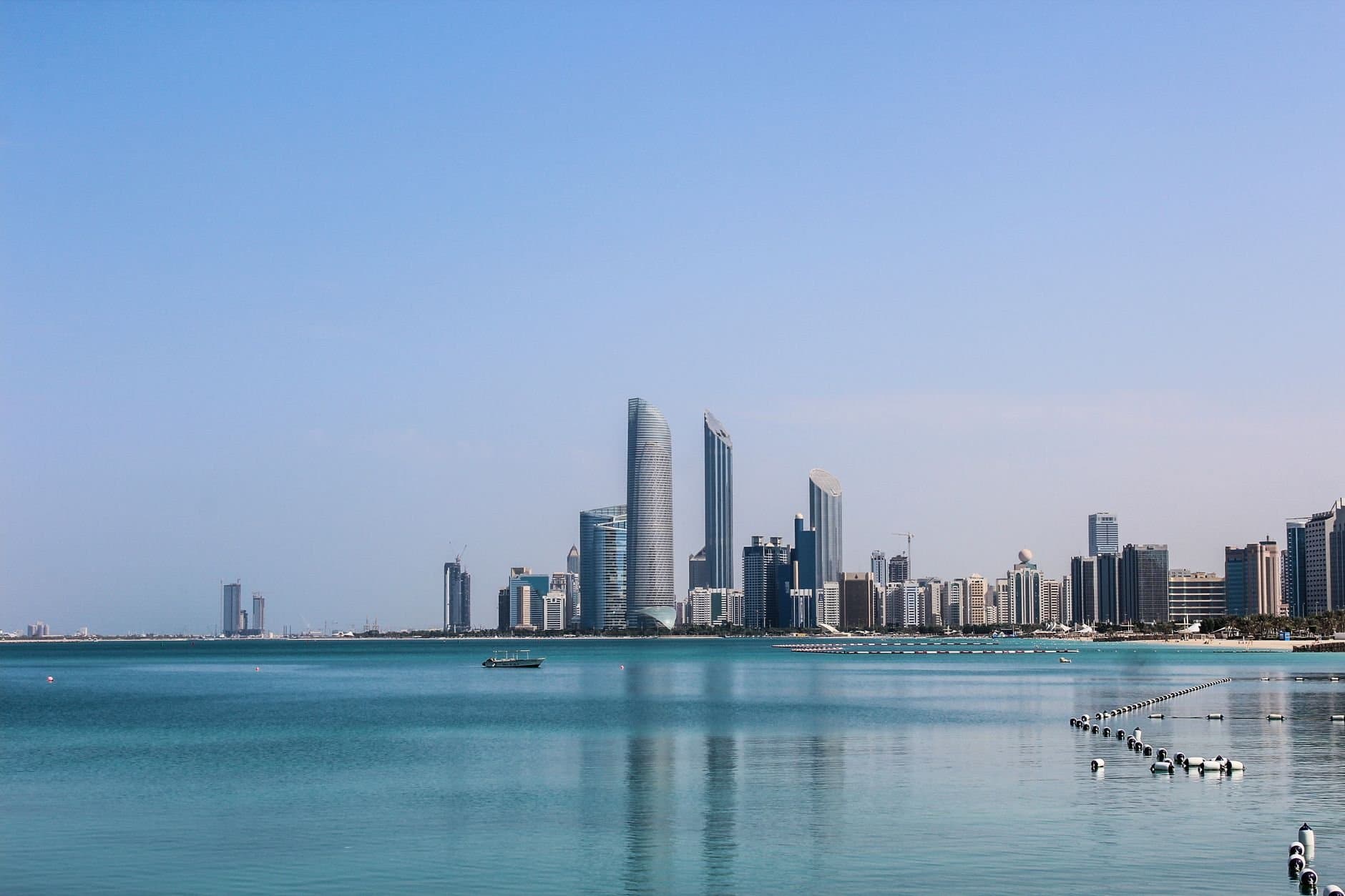Stunning view of the Abu Dhabi skyline reflecting in the calm Gulf waters on a sunny day.