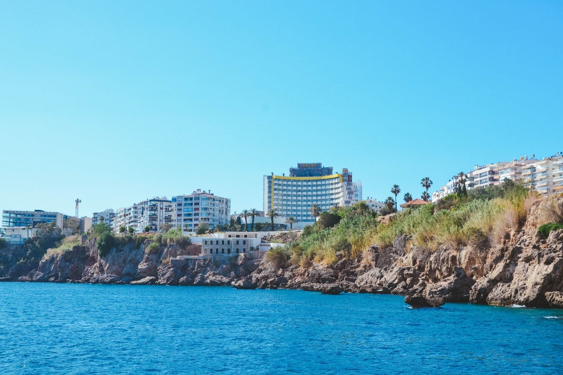 Beautiful Antalya coastline featuring modern buildings against a clear blue sky and crystal-clear sea.