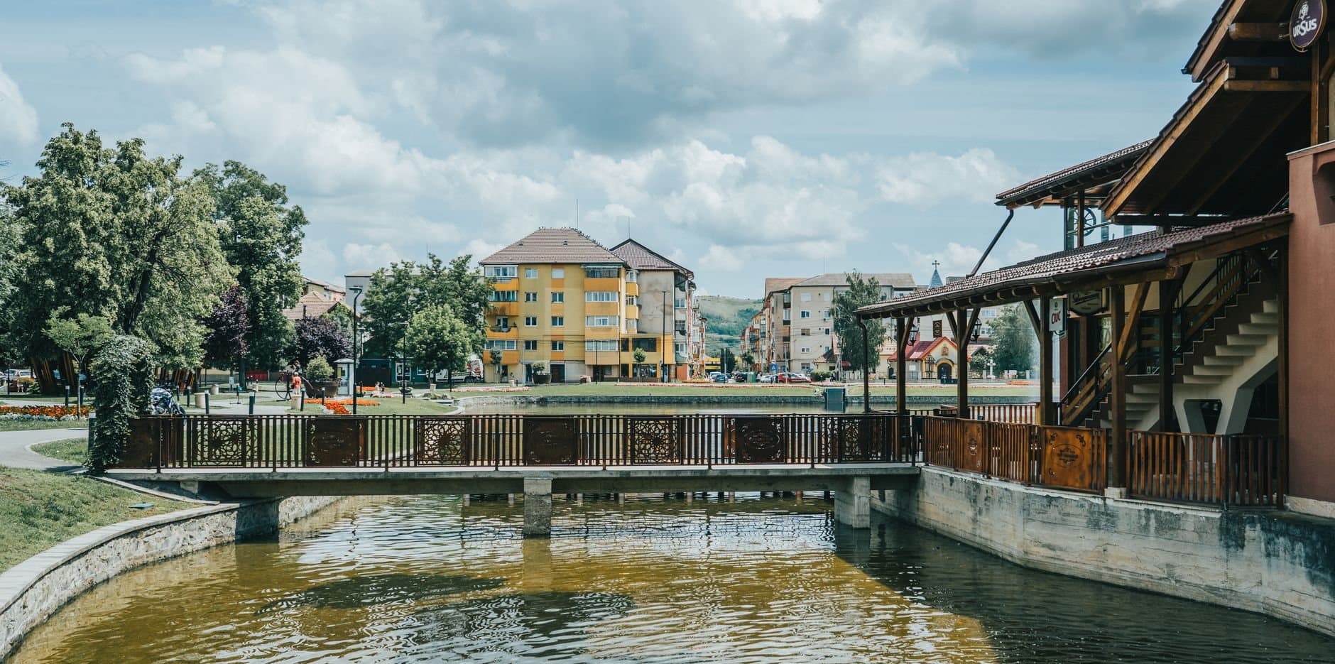 View of a quaint Romanian town with a bridge and colorful buildings under a cloudy sky.
