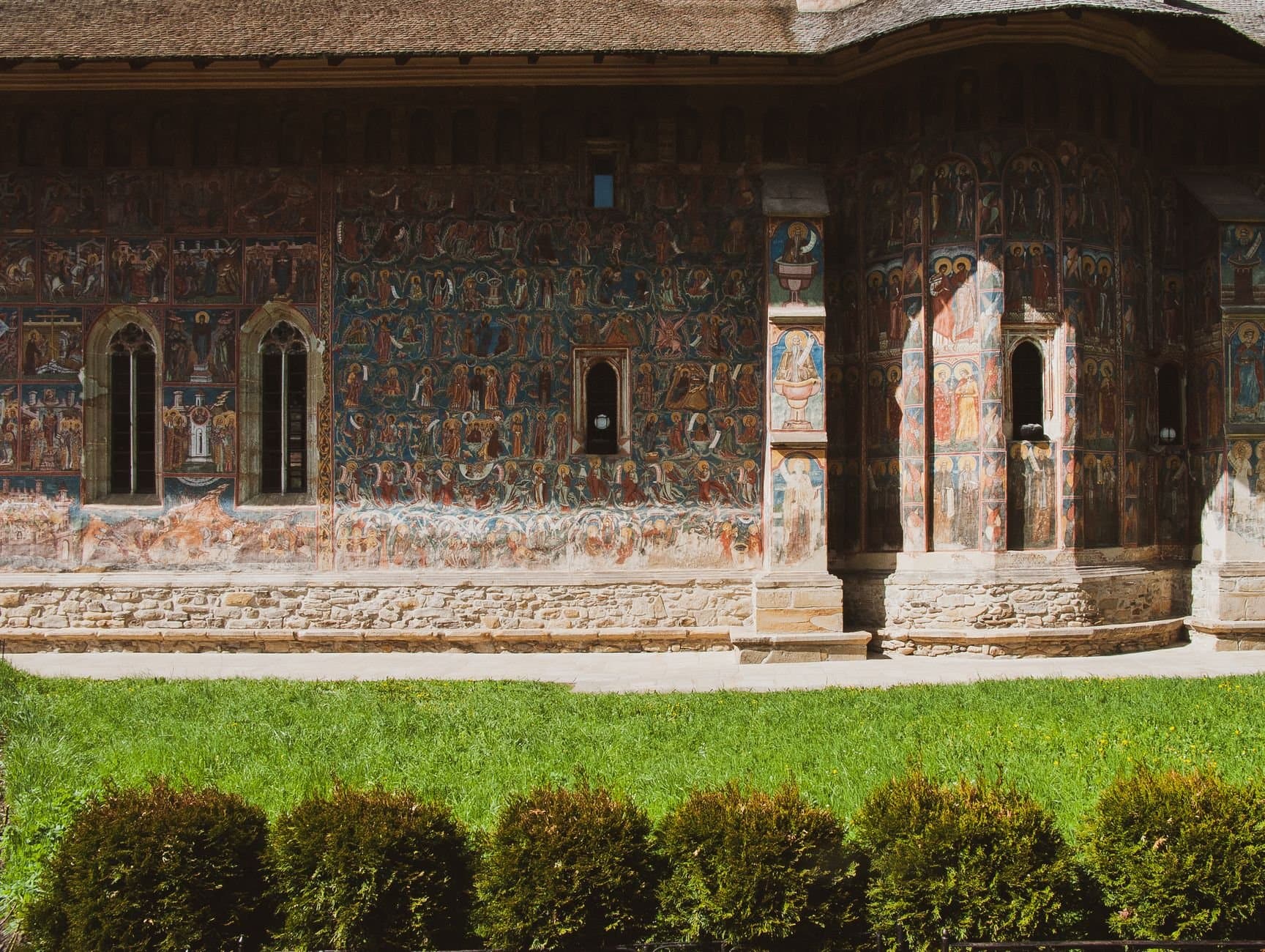 Exterior wall of an ancient monastery adorned with vibrant frescoes under sunny skies.