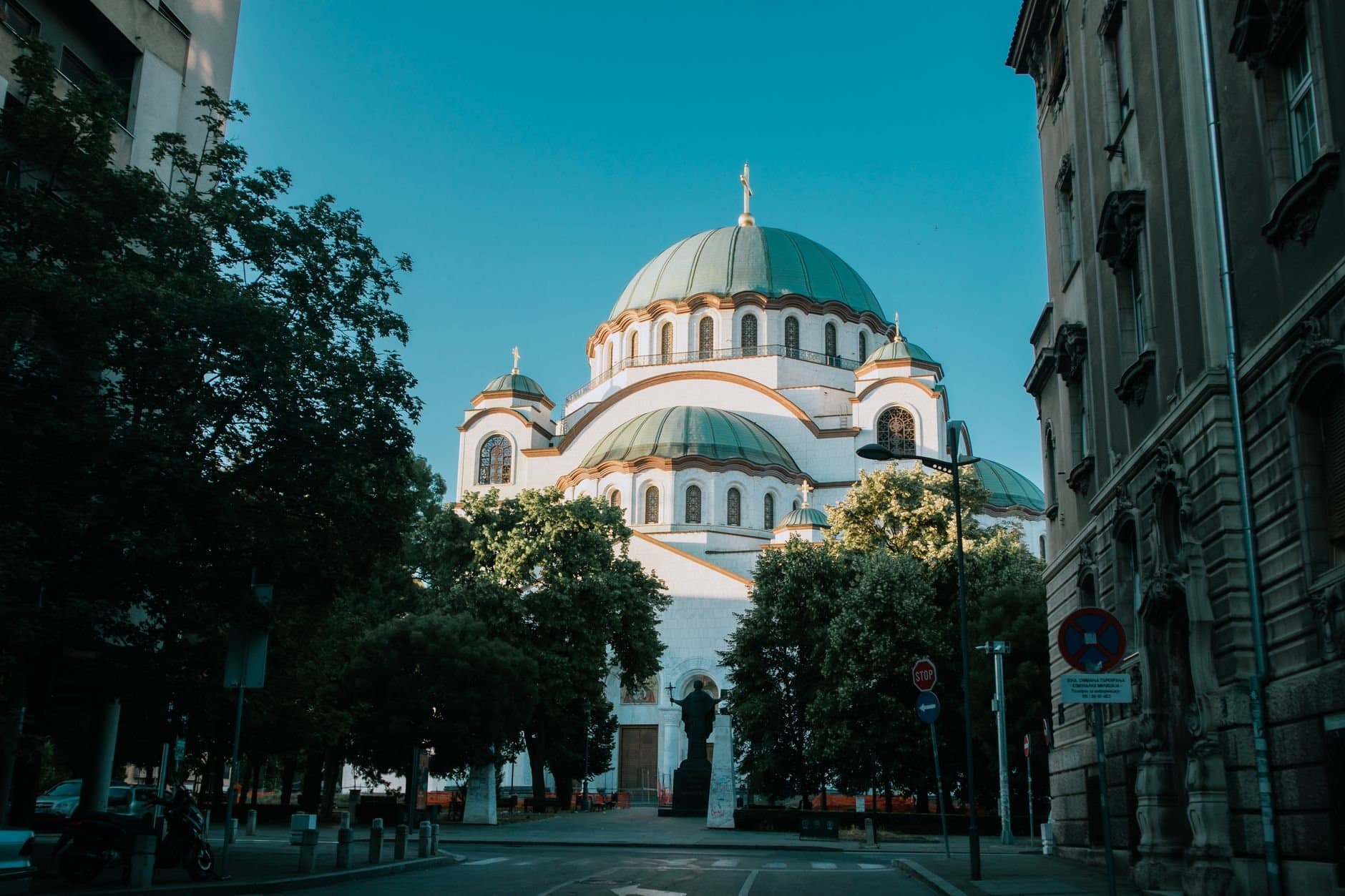 View of the iconic Saint Sava Temple in Belgrade on a sunny day, framed by trees and buildings.