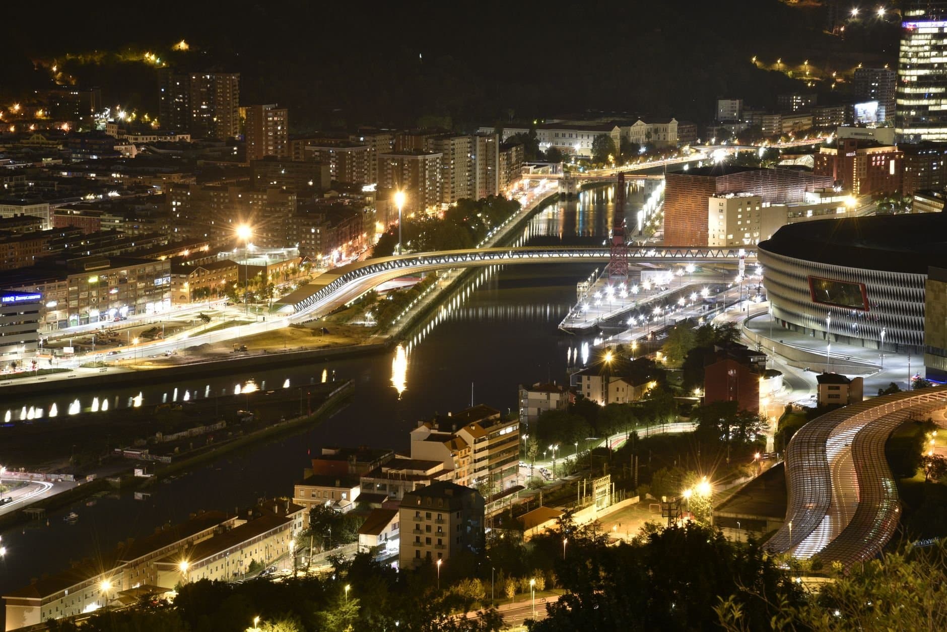 Aerial view of Bilbao cityscape illuminated at night, showcasing vibrant urban life.