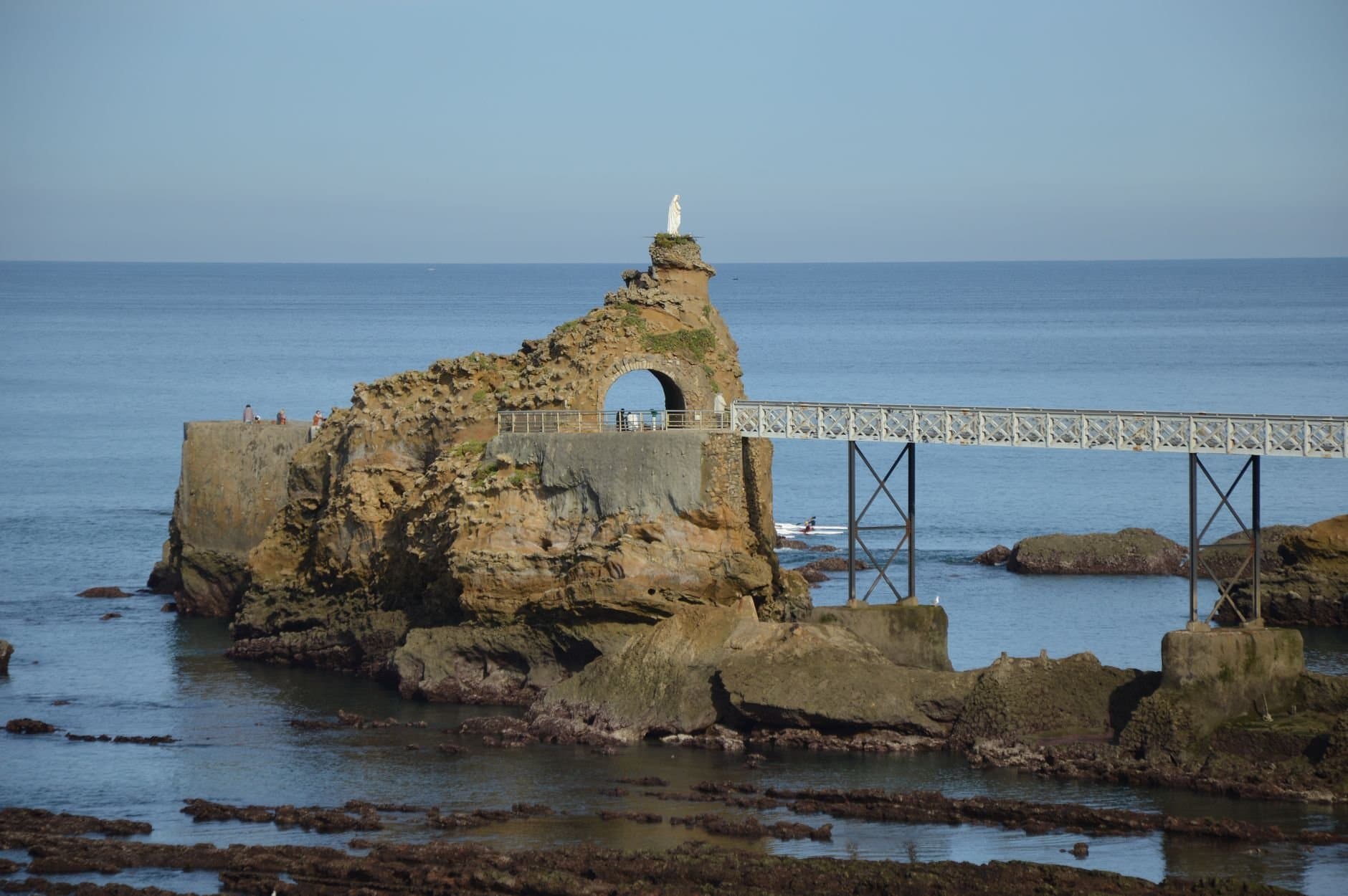 Rock formation with arch bridge and statue in Biarritz, overlooking the sea.