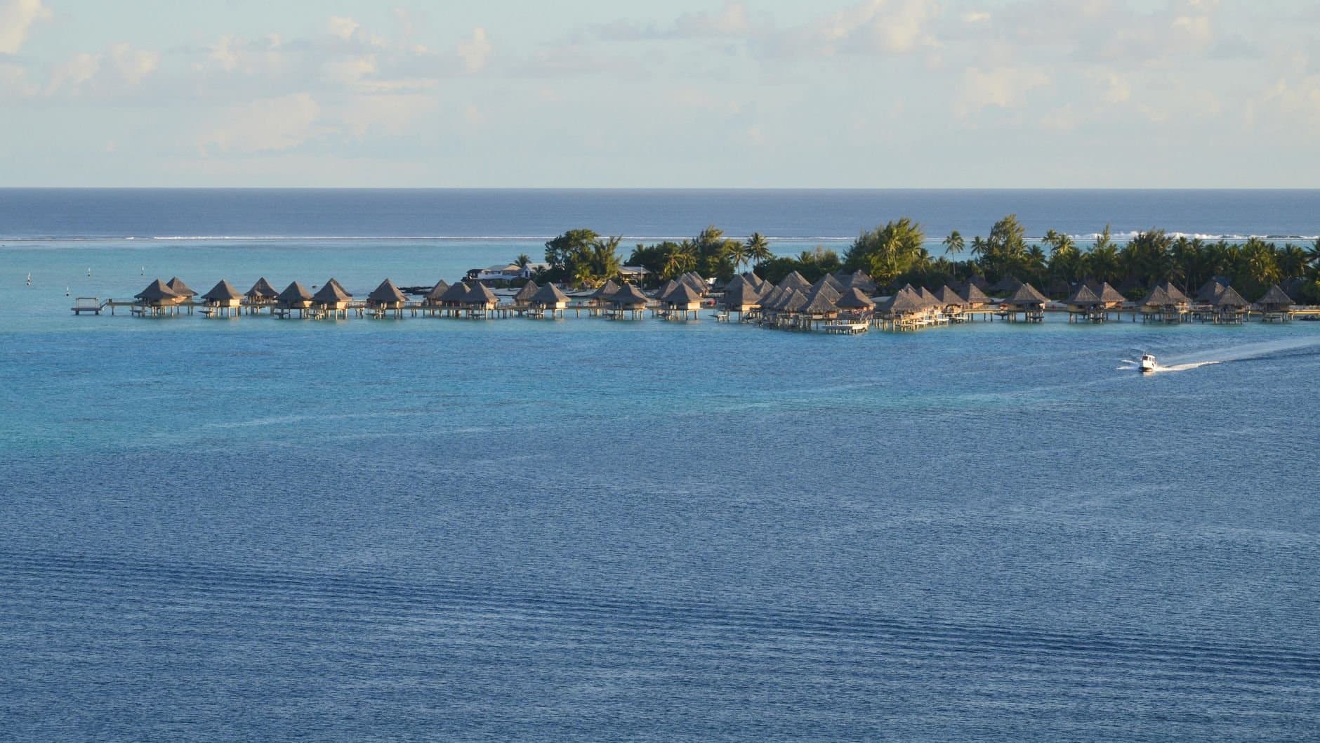 Overwater bungalows on a tropical island with clear blue sea and lush coast.