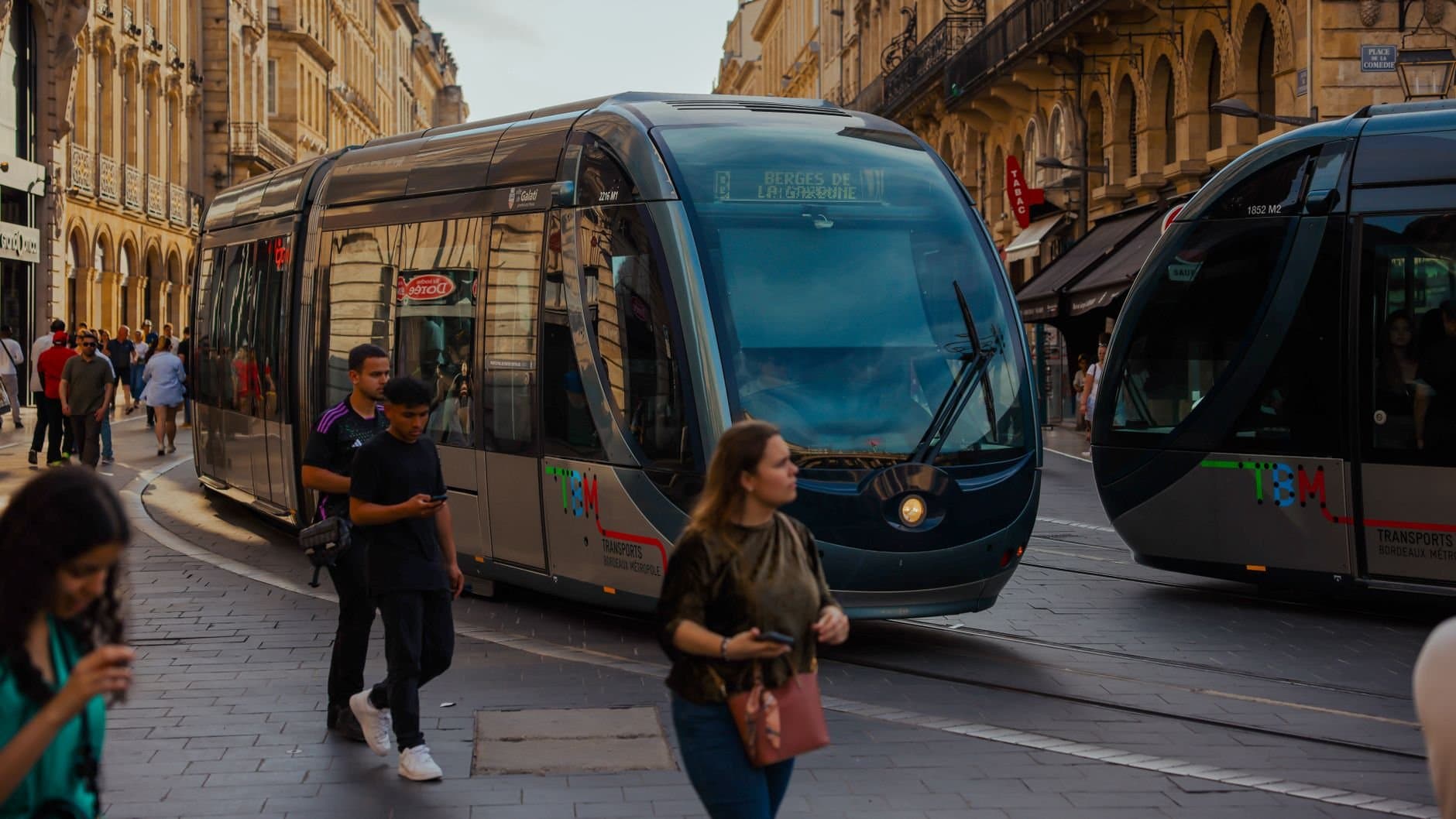 A bustling urban scene in Bordeaux featuring a sleek tram moving through lively streets.