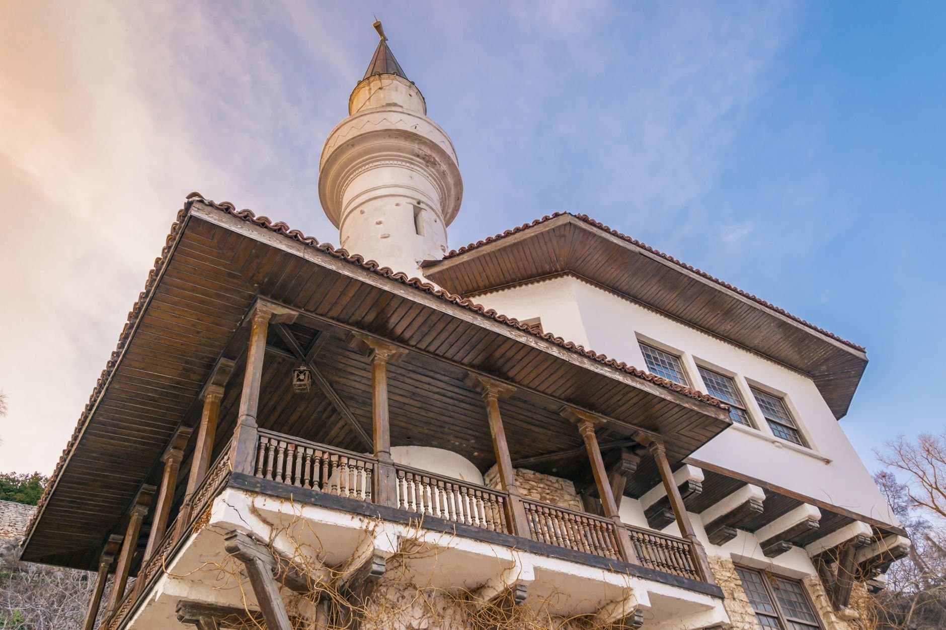 Low angle view of an architectural facade featuring a wooden balcony and tower against a blue sky.