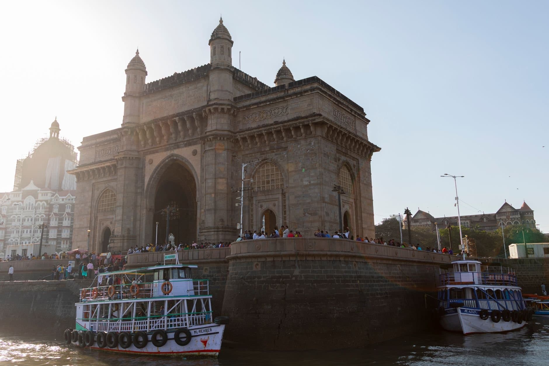 Stunning view of the iconic Gateway of India with boats and visitors at sunset in Mumbai.