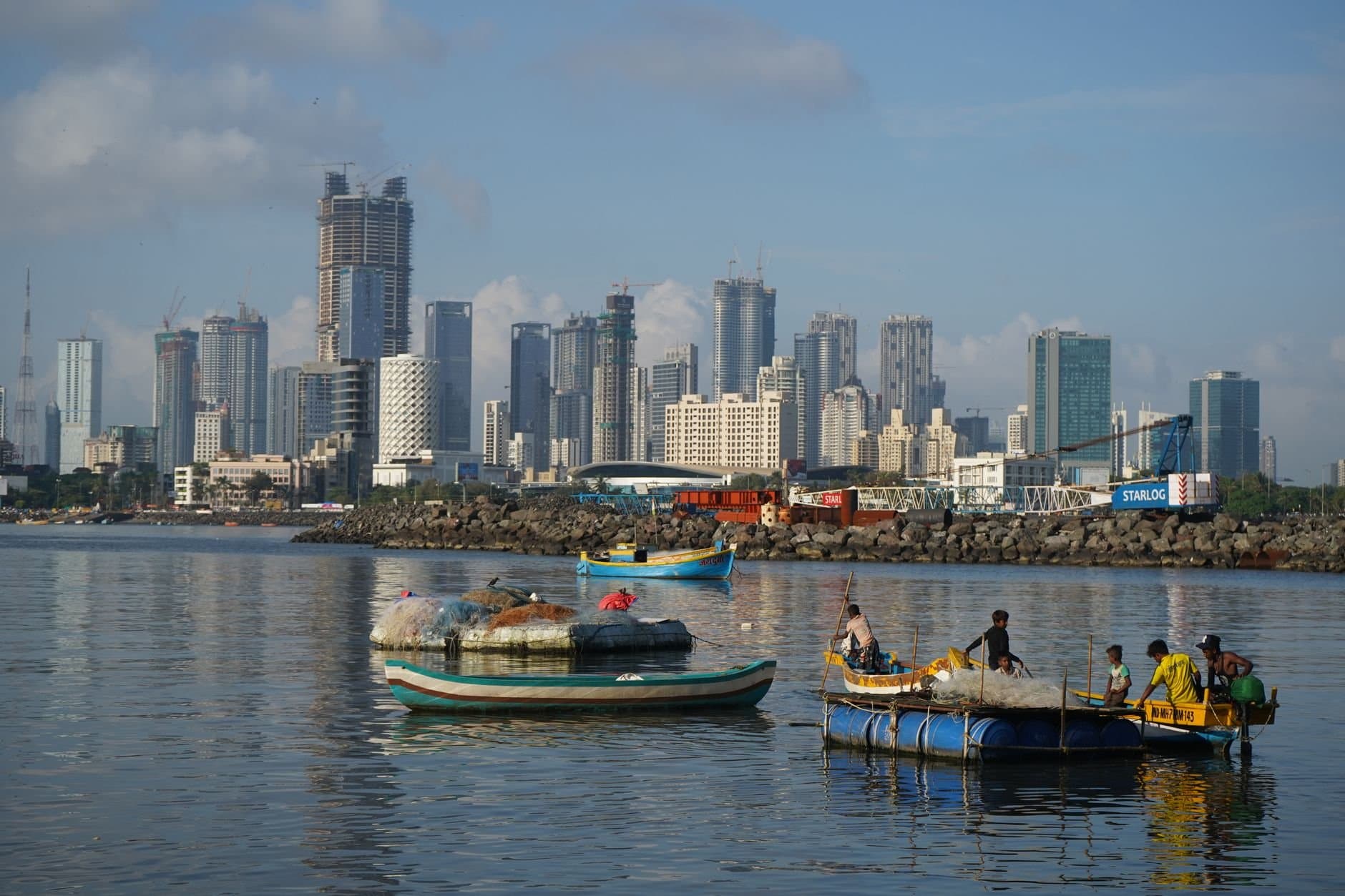 Vibrant view of Mumbai's skyline with local fishing boats on the water, capturing urban and traditional life.