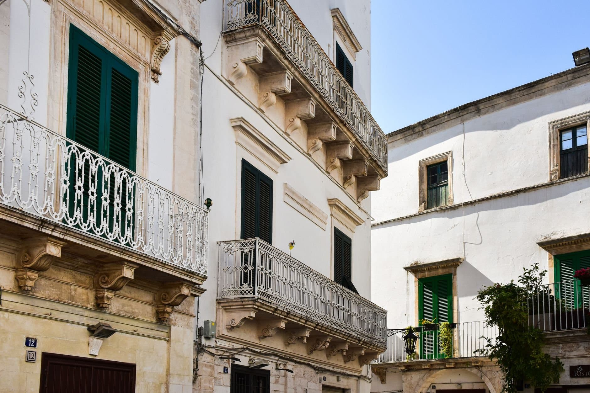 Charming white buildings with ornate balconies in a sunlit Italian street.