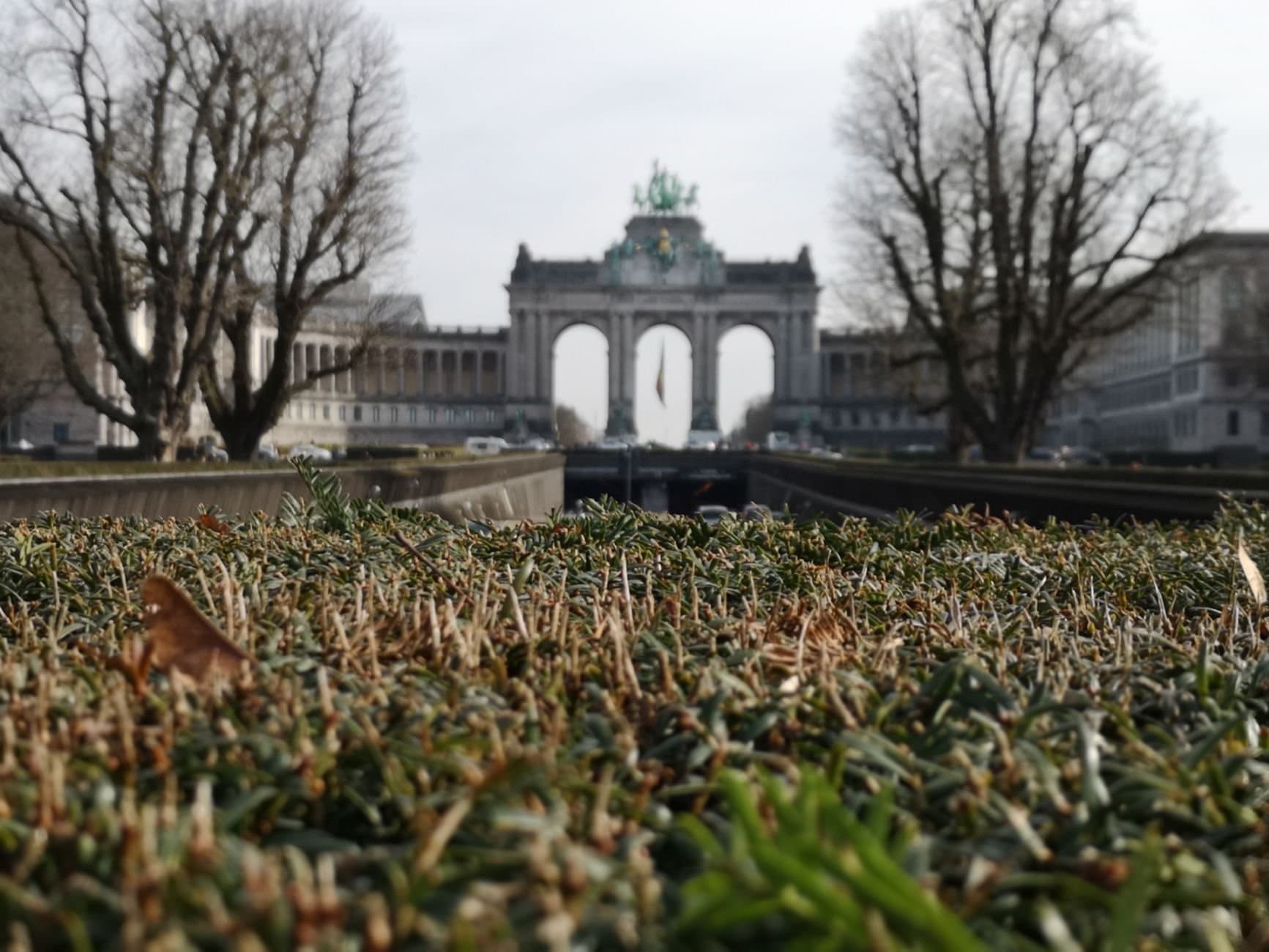 The iconic Triumphal Arch in Brussels with grass in the foreground, captured outdoors on a winter day.