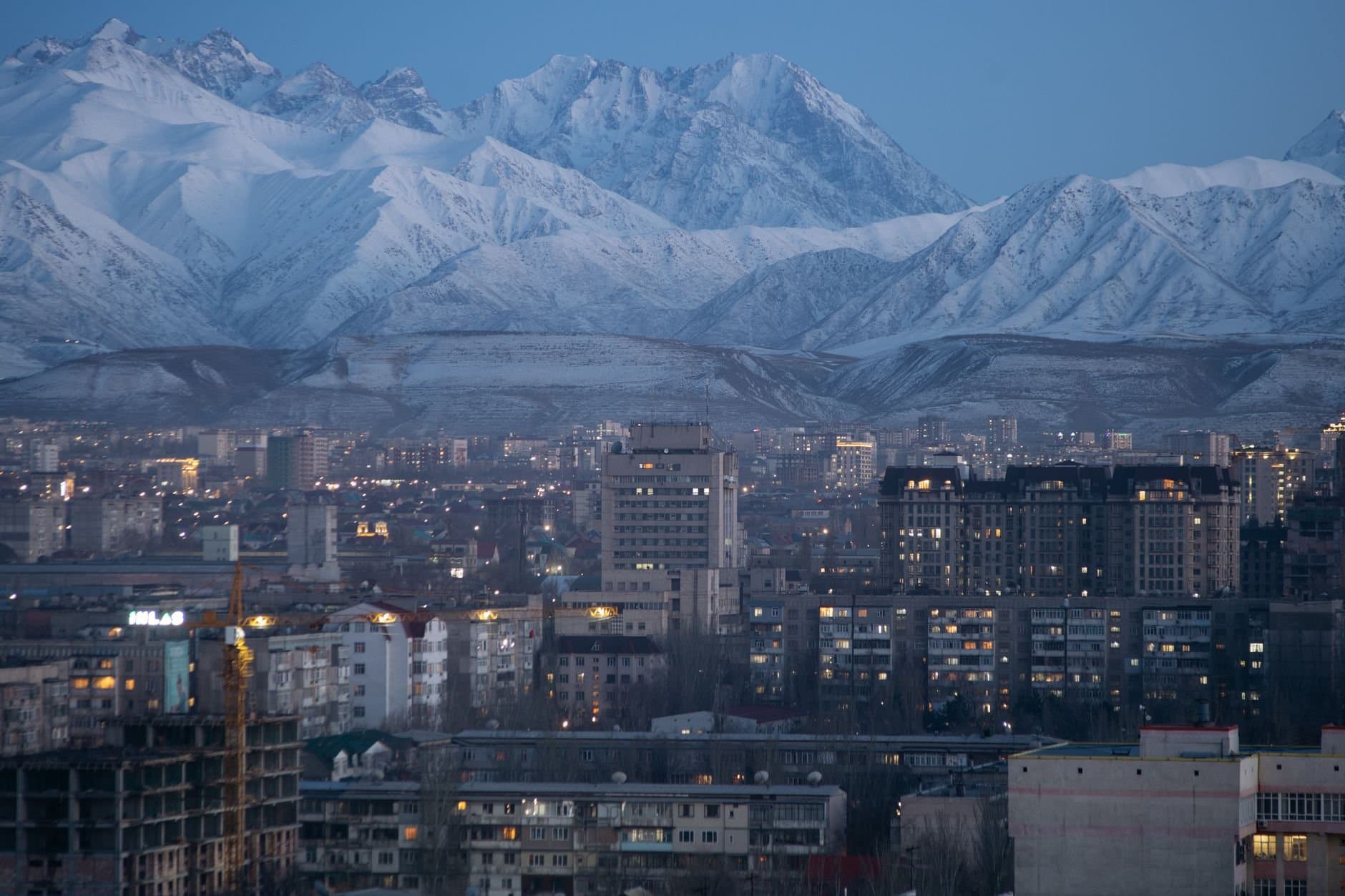 Stunning aerial view of Bishkek city against a backdrop of snow-covered mountains during twilight.