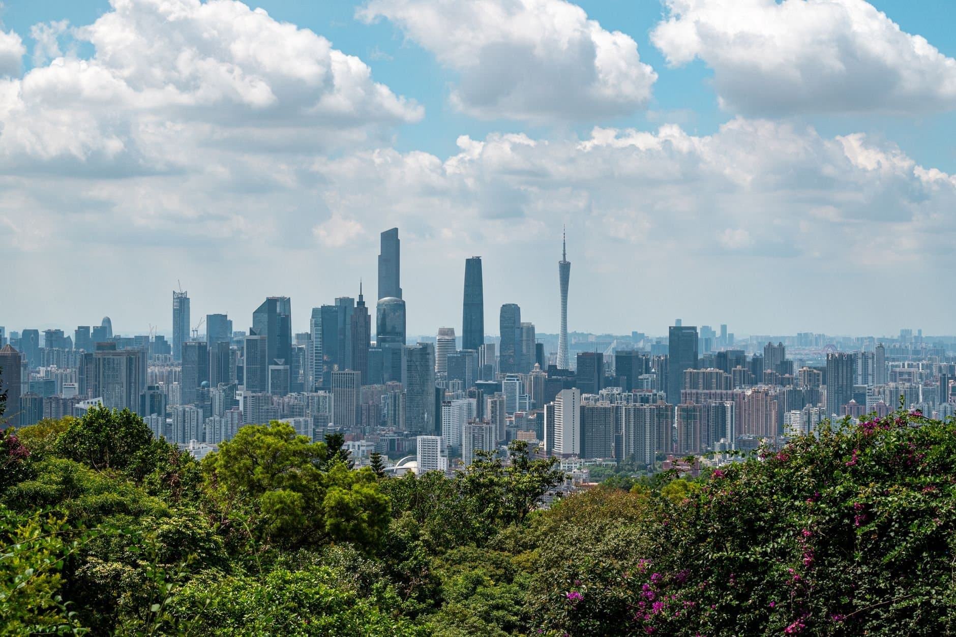 Breathtaking view of Guangzhou cityscape with skyscrapers and vibrant greenery under a cloudy sky.