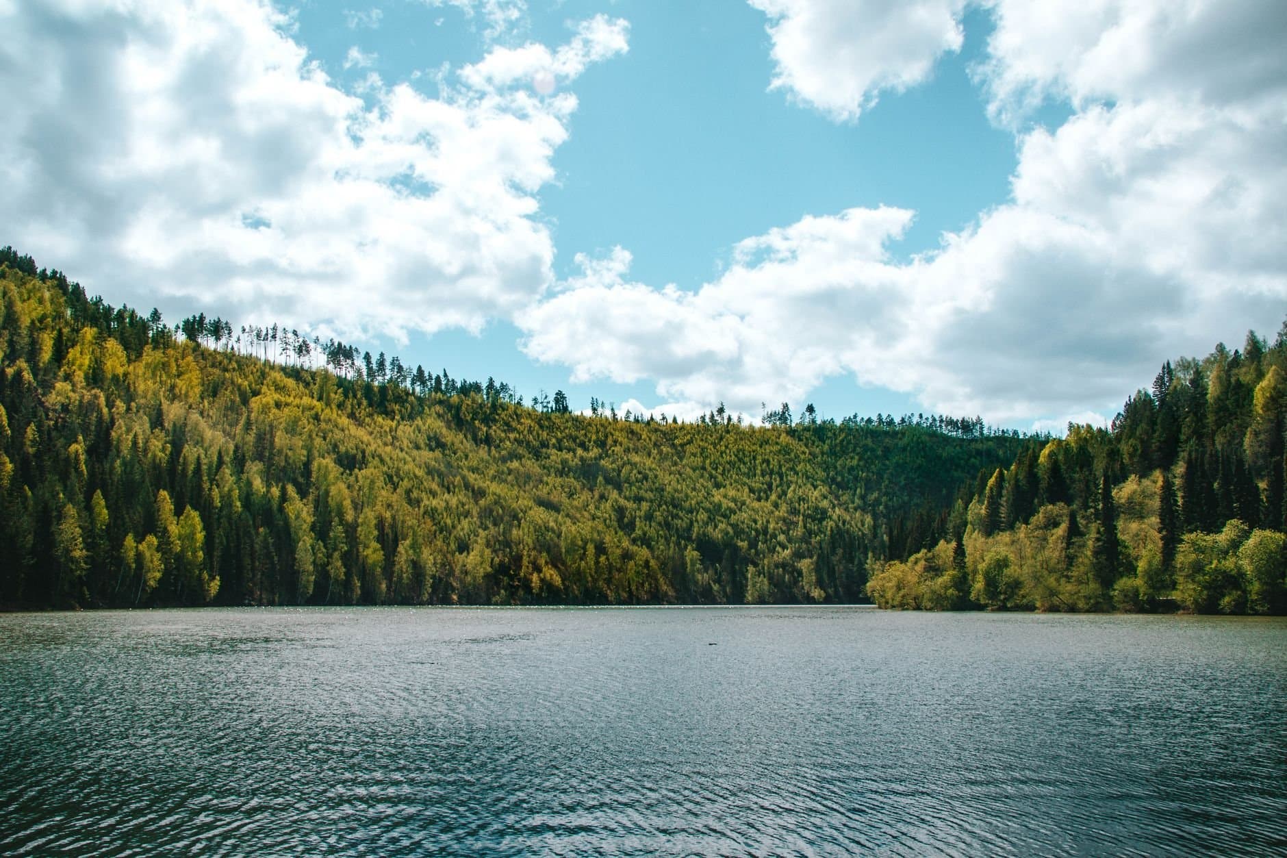 Beautiful lake surrounded by lush forest under a bright sky in Sim, Russia.